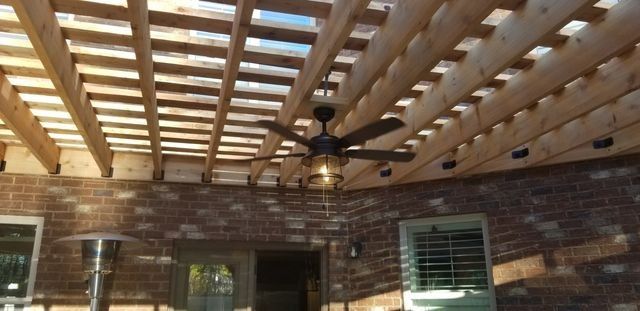 Outdoor patio with a wooden pergola ceiling, brick walls, and a ceiling fan with lights.