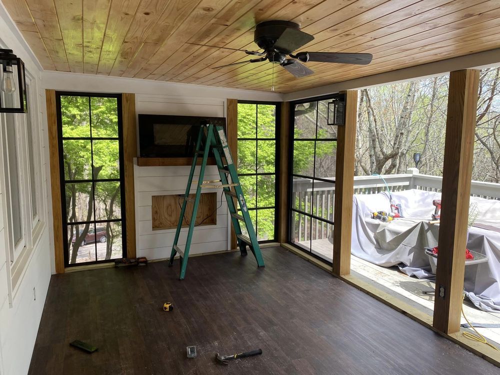 Sunroom interior with dark wood floor, large black-framed windows, and a wooden ceiling.