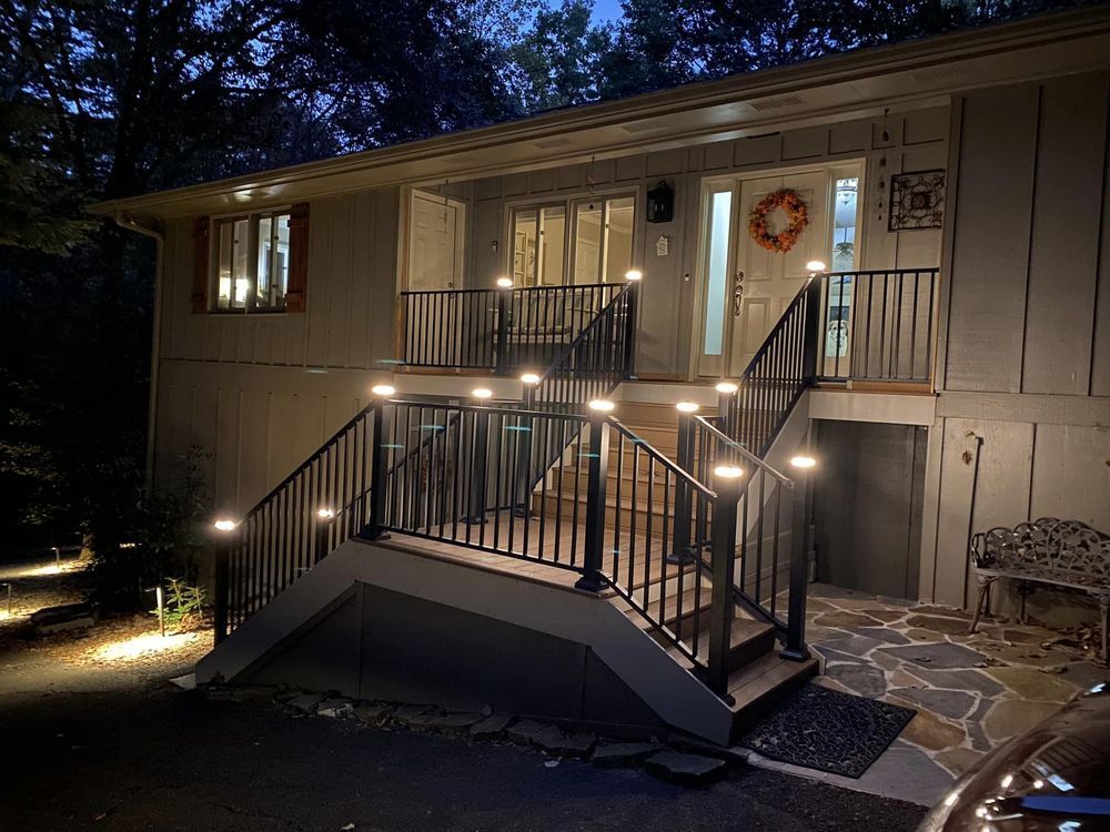Night exterior of a two-story house with illuminated stair railings, front door, and landscape lighting.