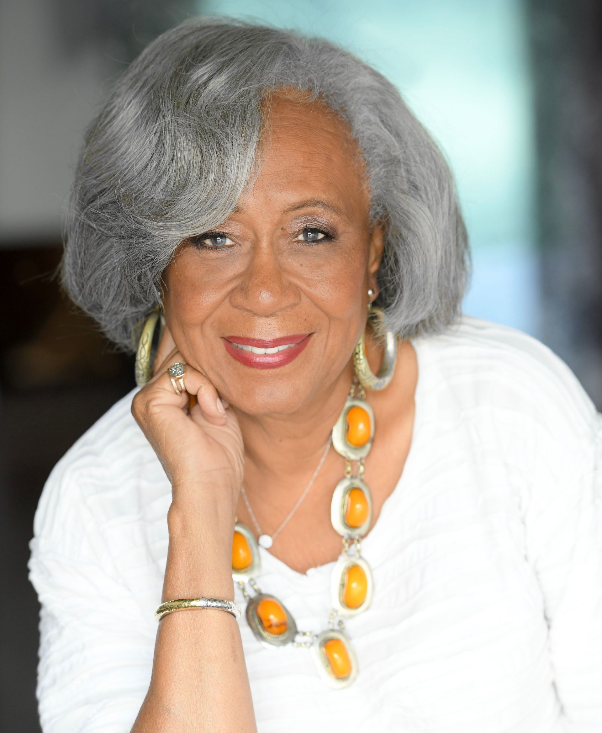 A woman with gray hair and red lipstick is smiling for the camera.