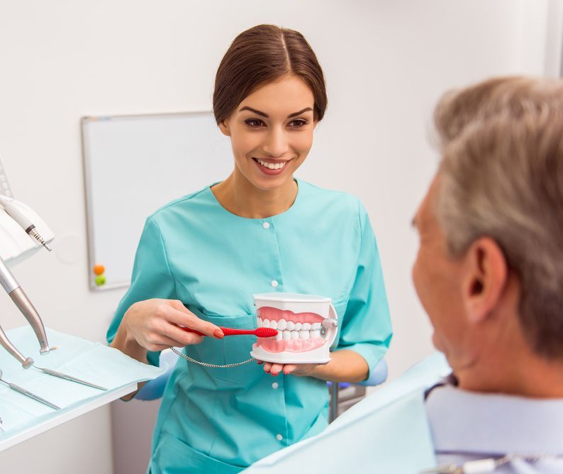 Dentist Holding The Denture With Toothbrush — Smiles on Hobart In Hobart TAS