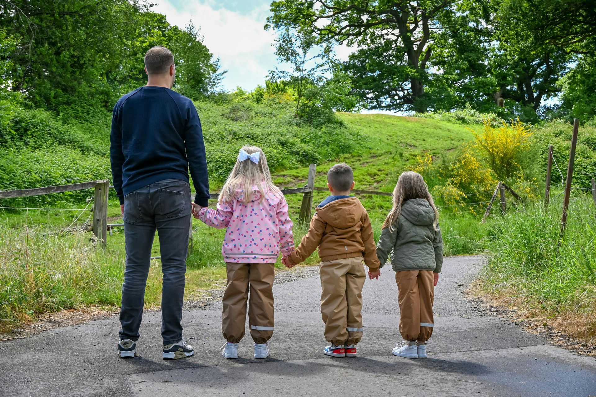 A man and three children are walking down a path holding hands.