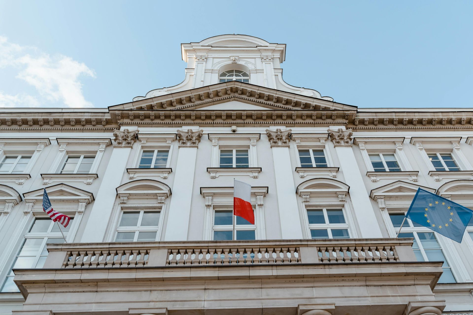 A large white building with a balcony and flags on it.