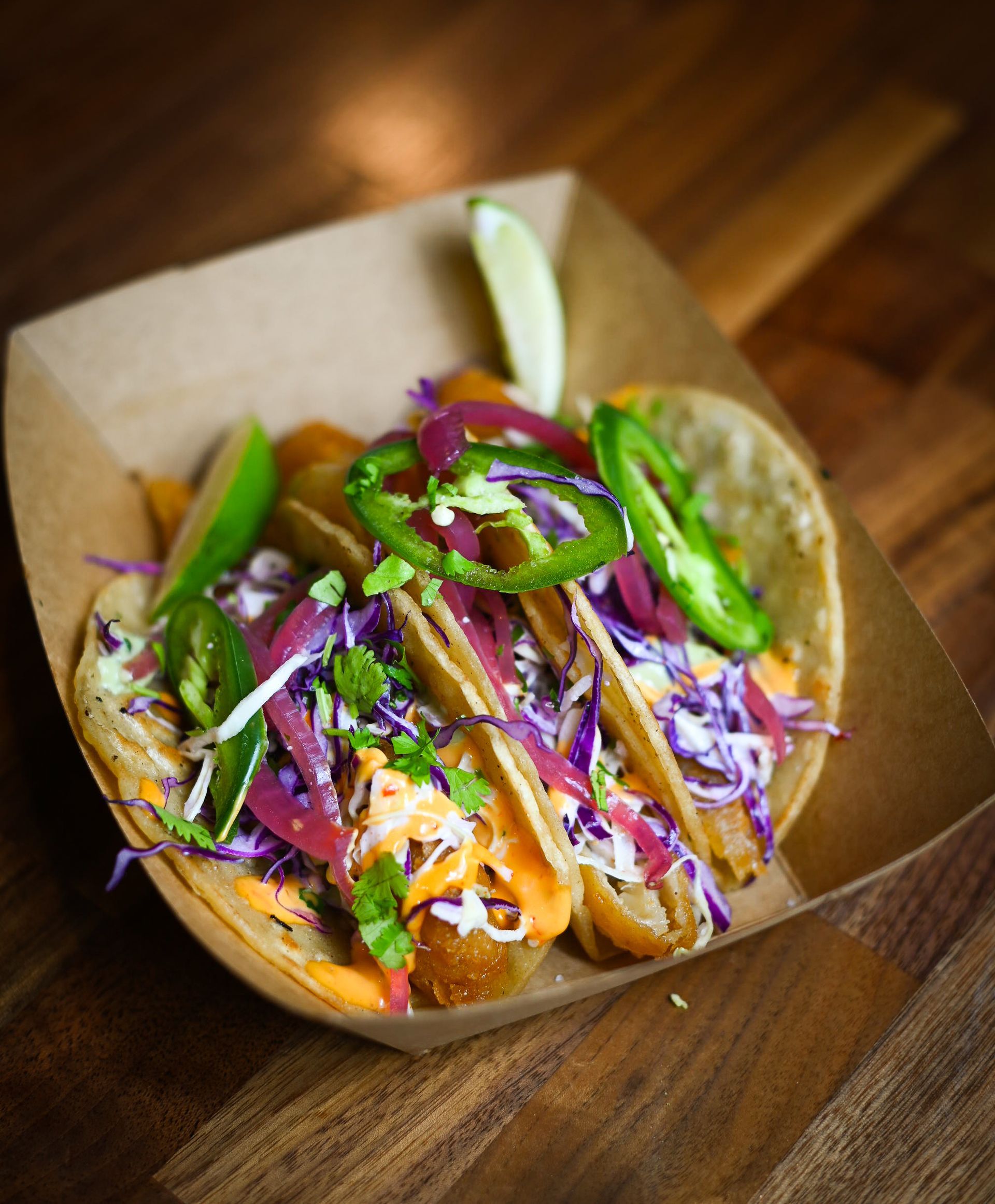 A paper container filled with tacos and vegetables on a wooden table.