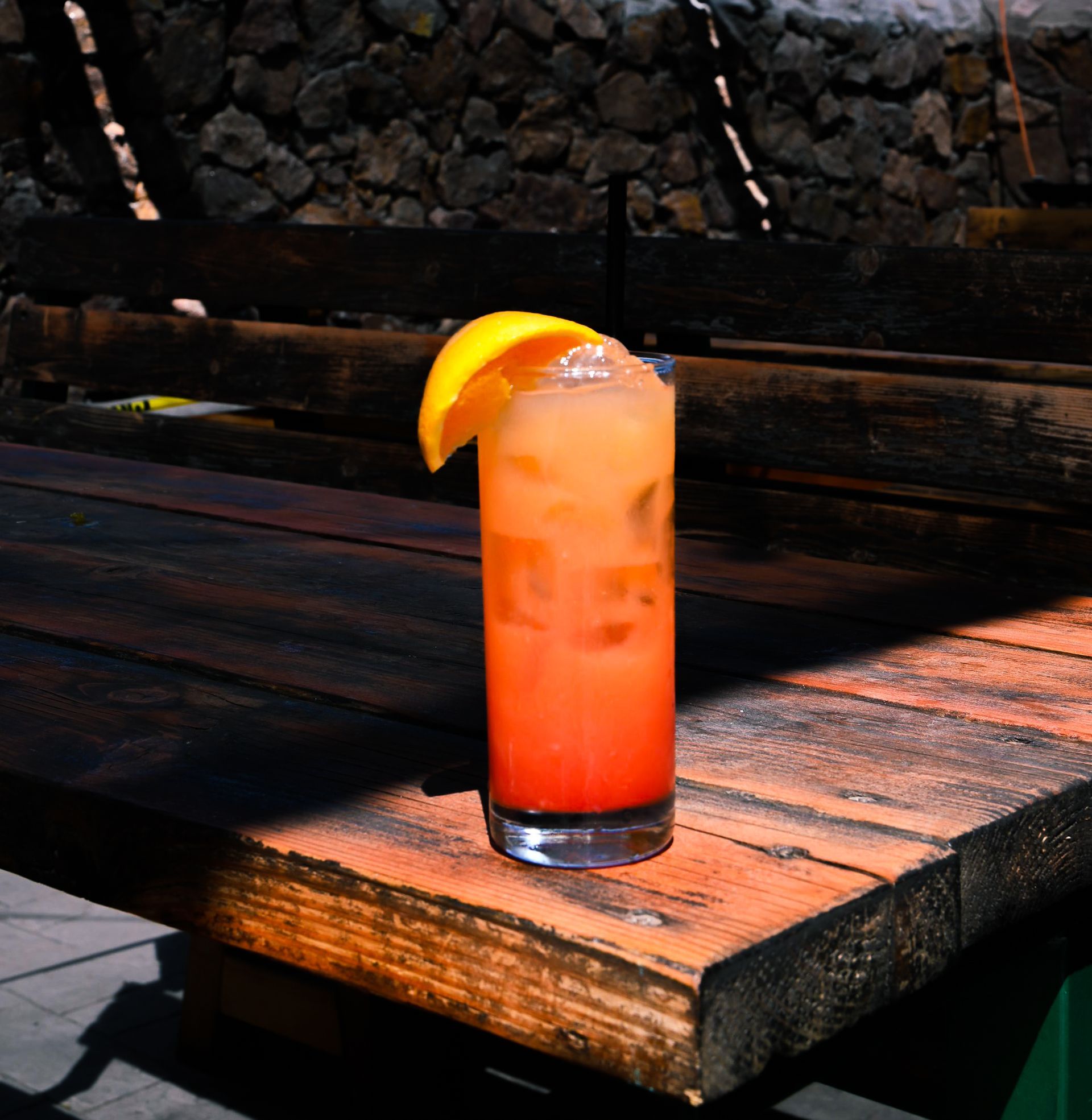 A tall glass of orange drink with a slice of lemon on a wooden table