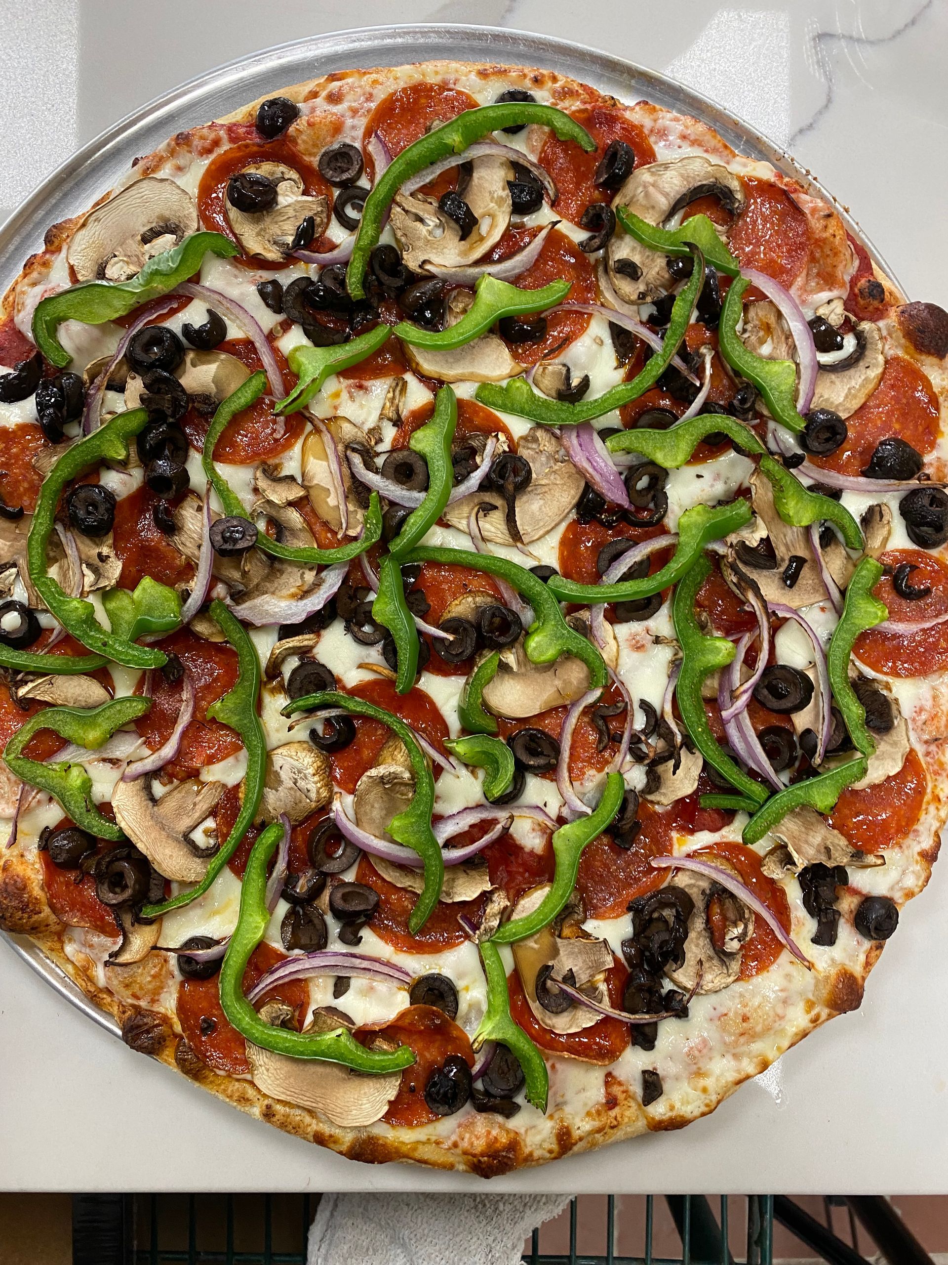A pizza with pepperoni , olives , peppers , onions and mushrooms on a pan.