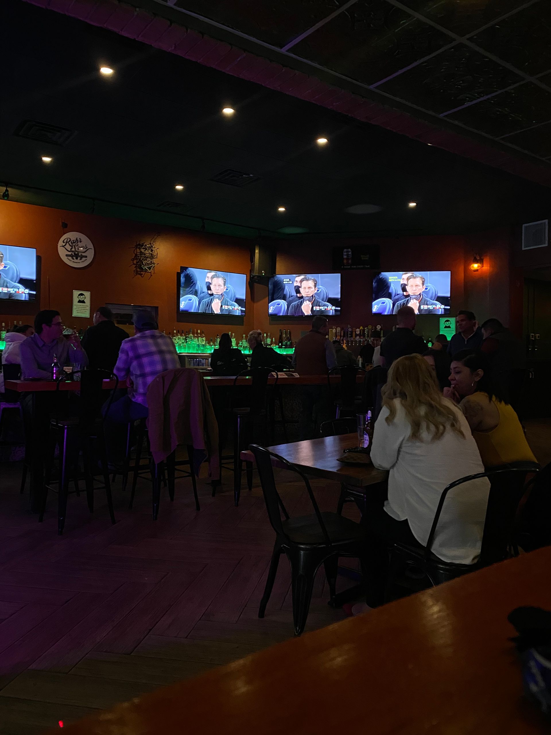 A group of people are sitting at tables in a bar watching television.