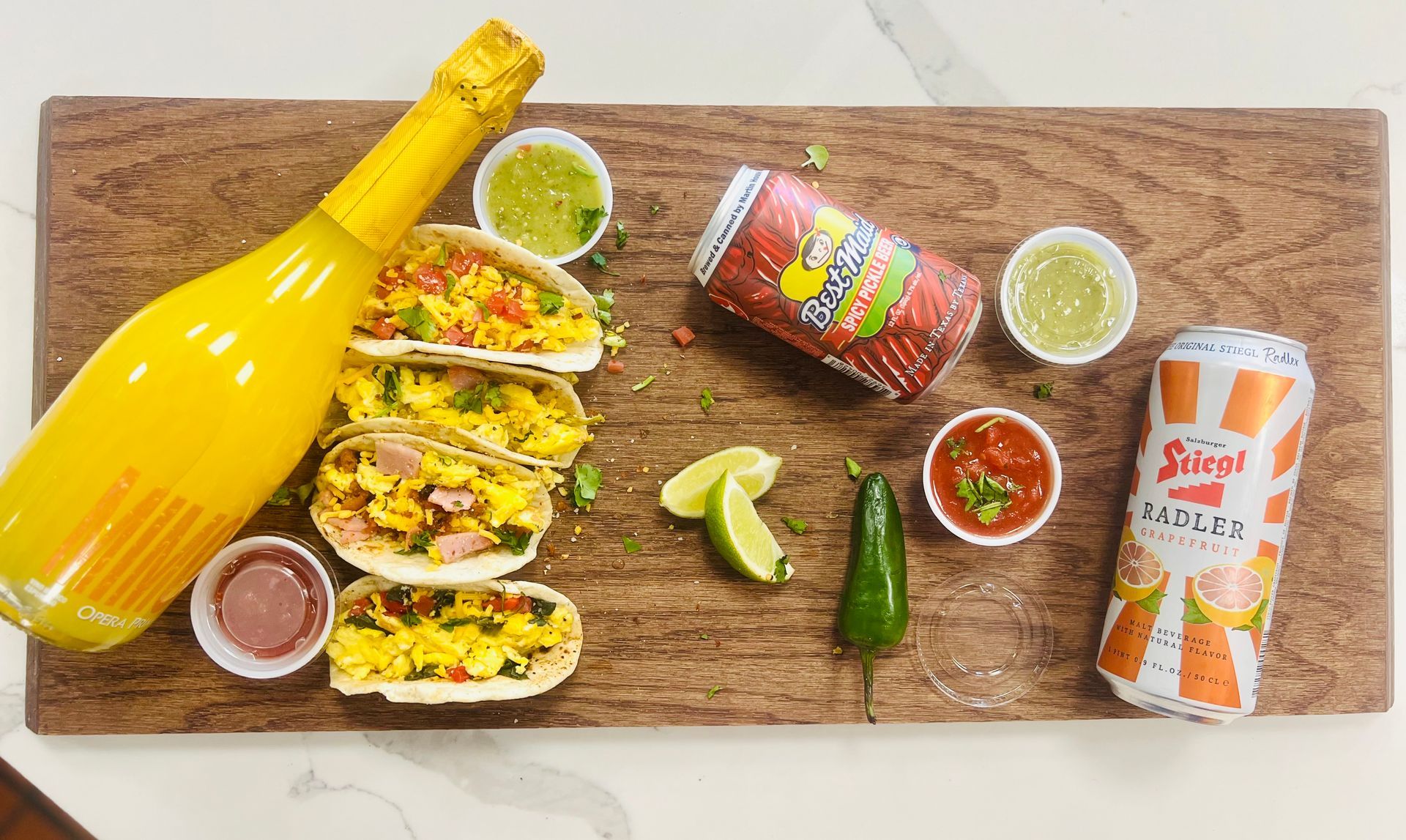 A wooden cutting board topped with tacos , a bottle of orange juice and a can of soda.