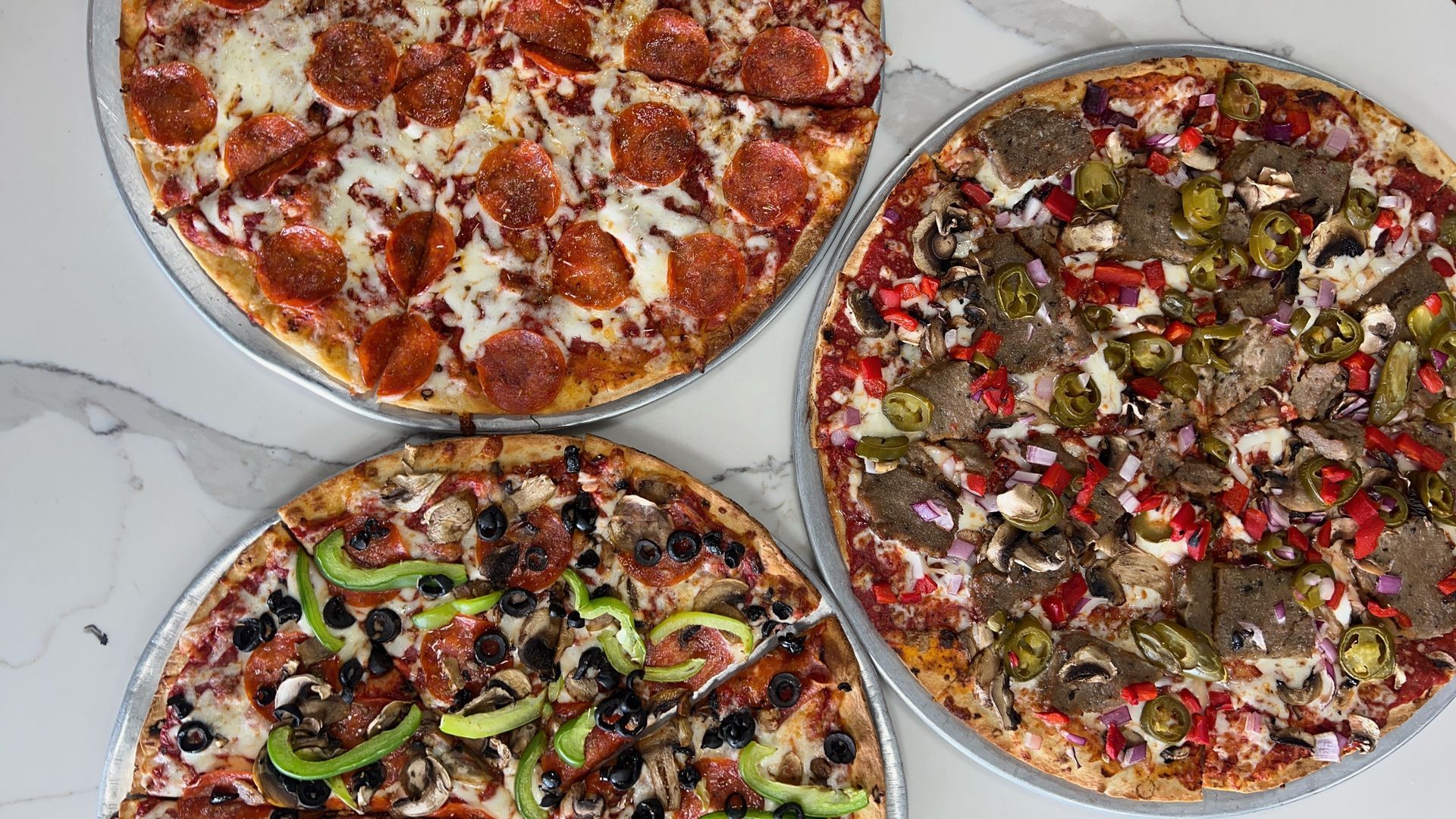 Three pizzas with different toppings are sitting on a table.