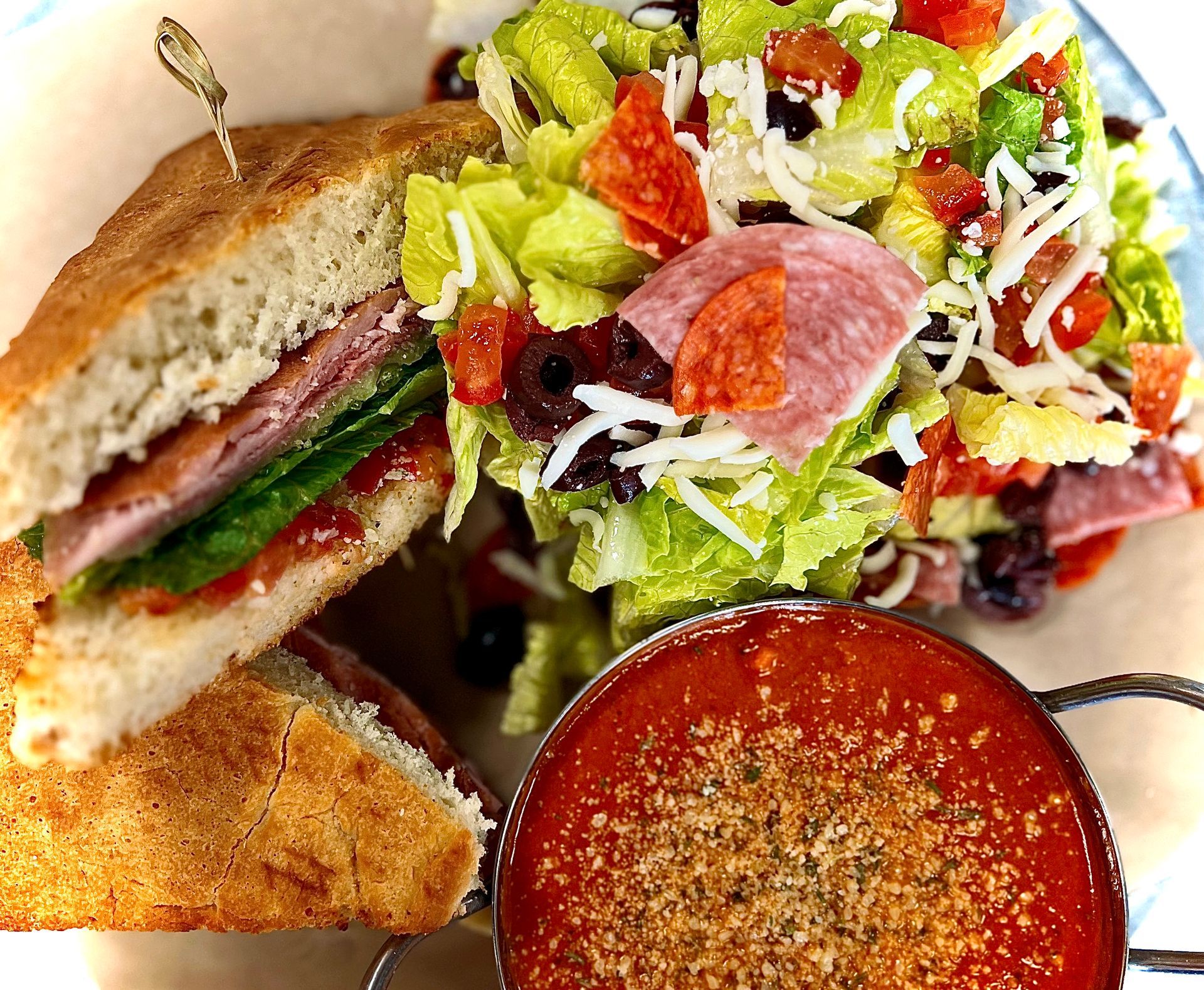 A sandwich and a salad are on a plate next to a bowl of soup.