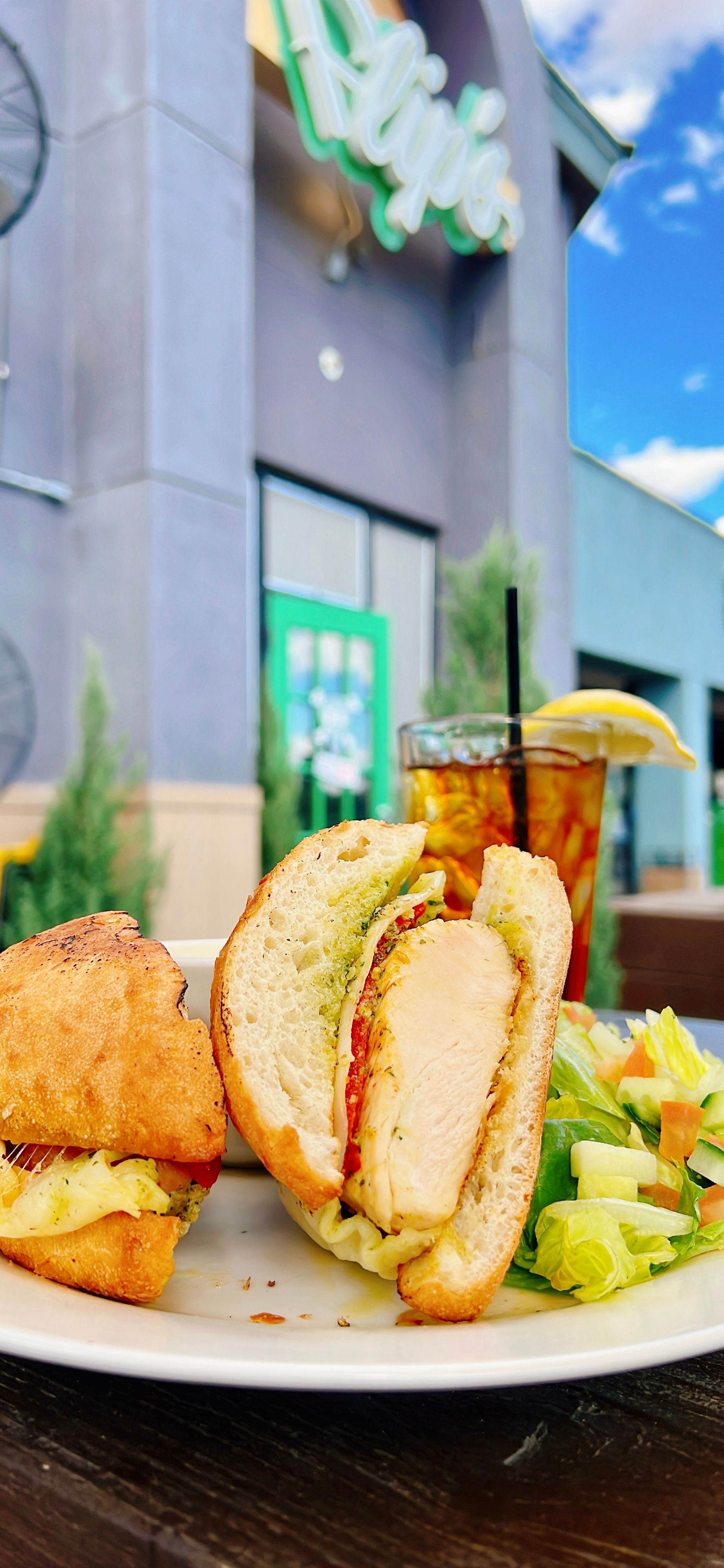 A close up of a plate of food with a sandwich and a drink on a table.