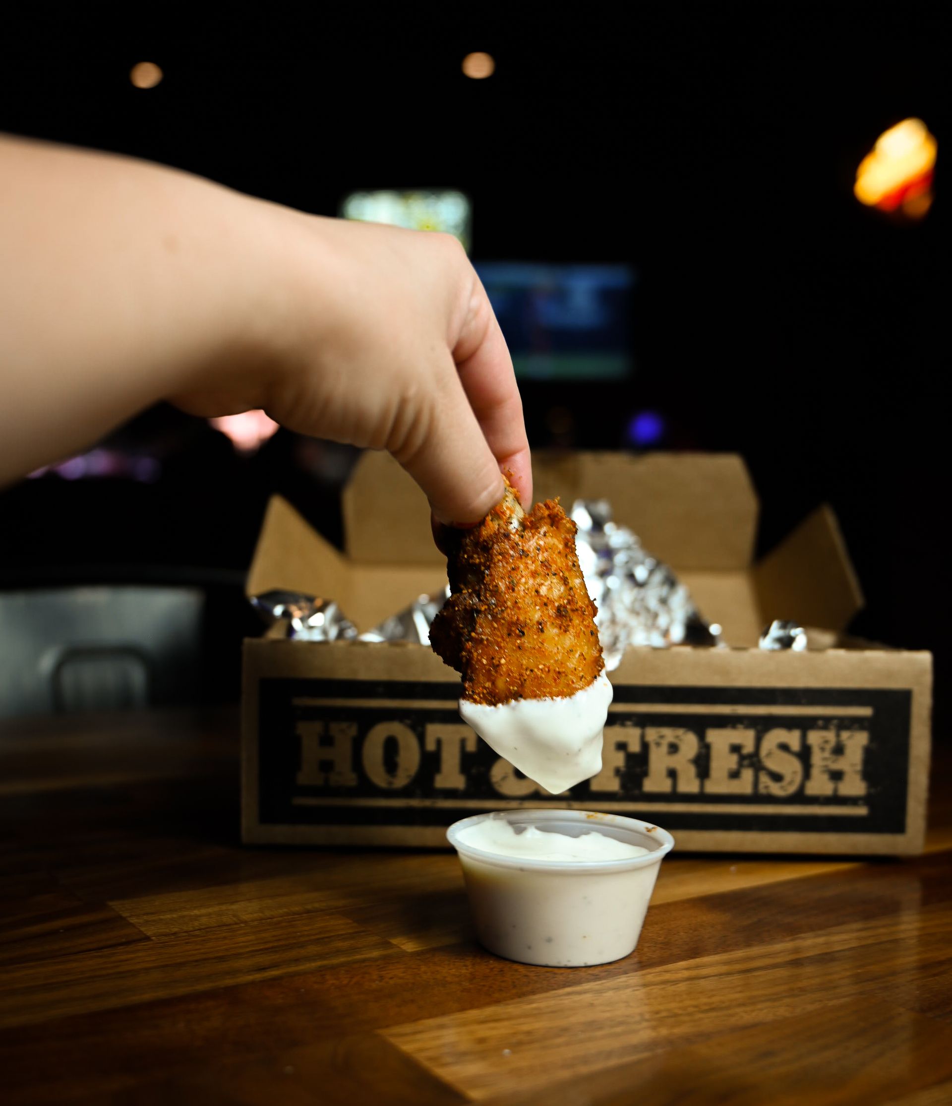 A person dipping a chicken wing in ranch sauce