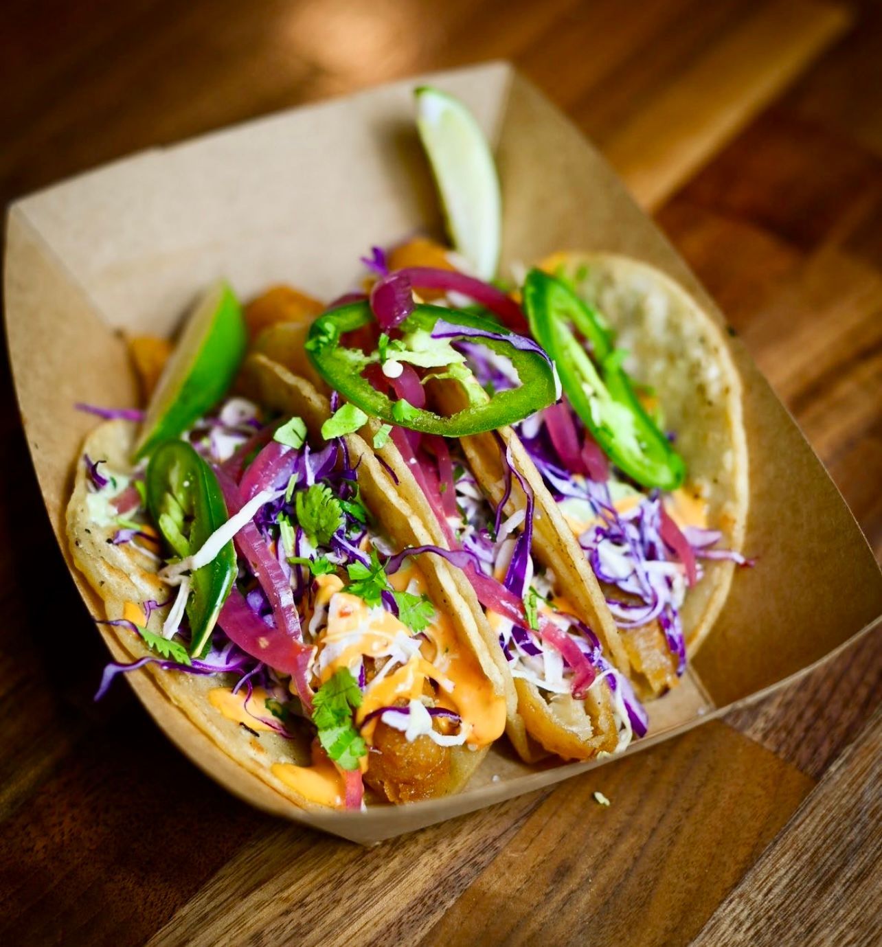 A paper container filled with tacos and vegetables on a wooden table