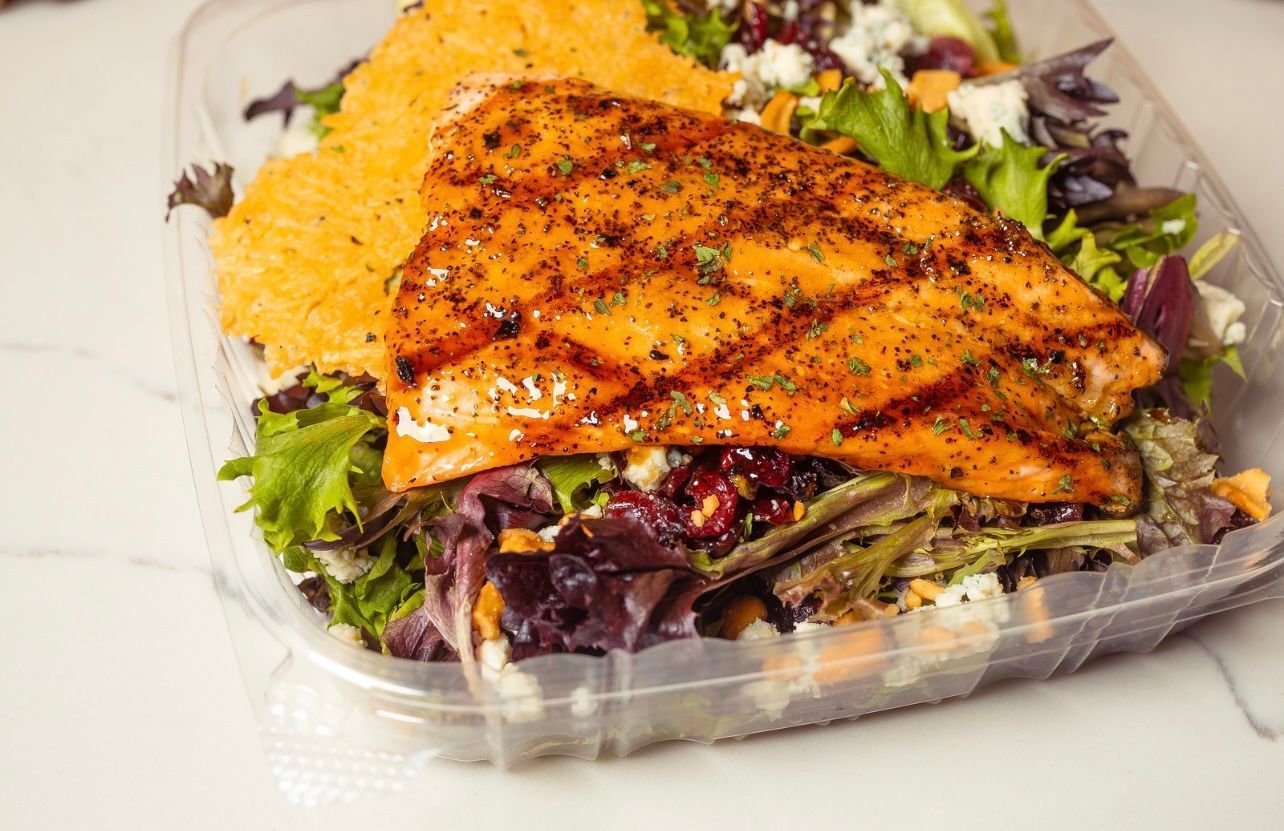 A plastic container filled with a salad and a piece of grilled salmon.