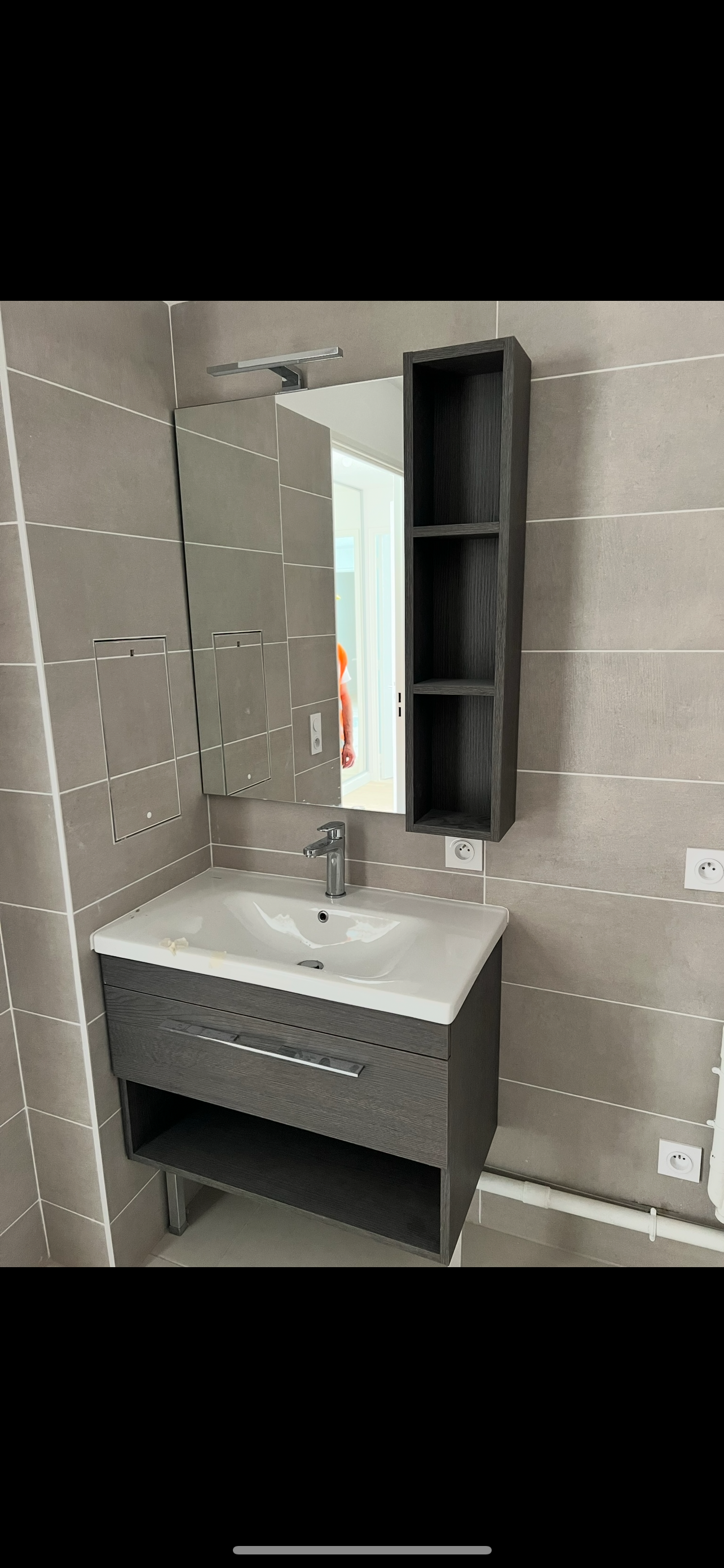 Meuble de salle de bain gris avec miroir et étagère de rangement.