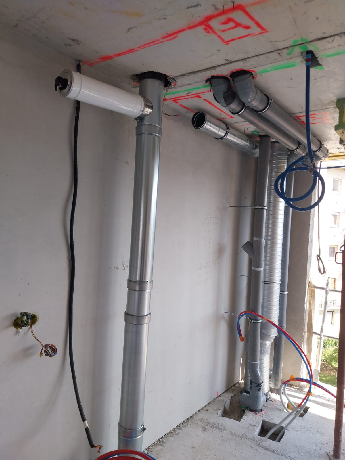 Tuyaux et conduits installés sur un chantier, avec marquages ​​rouges et verts au plafond.