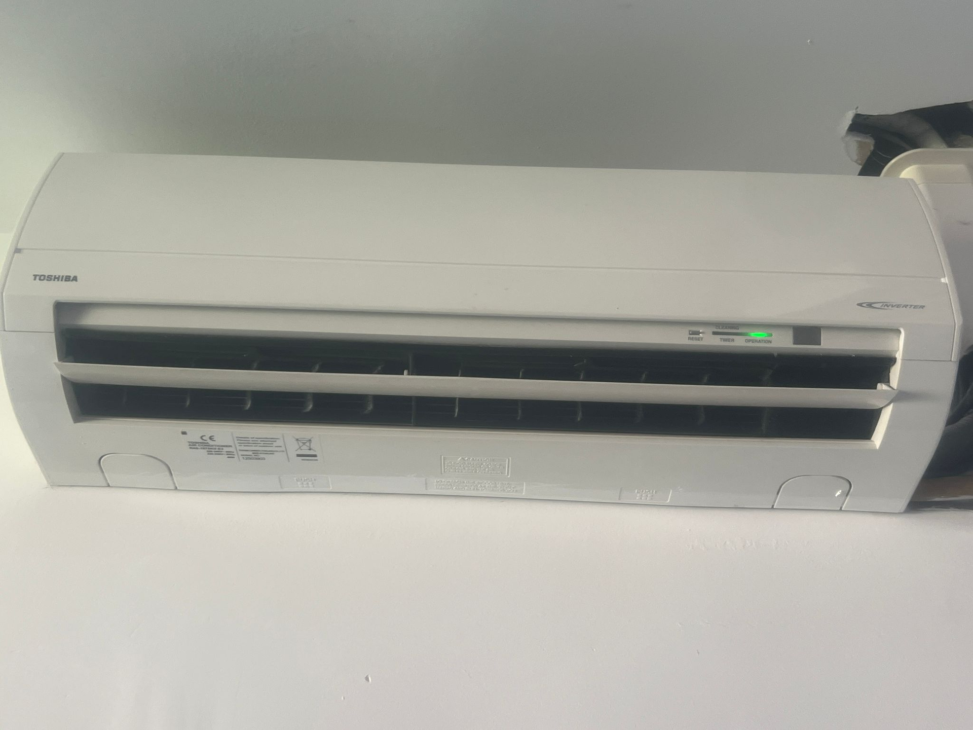 Un climatiseur Toshiba blanc monté sur un mur, avec des évents visibles.