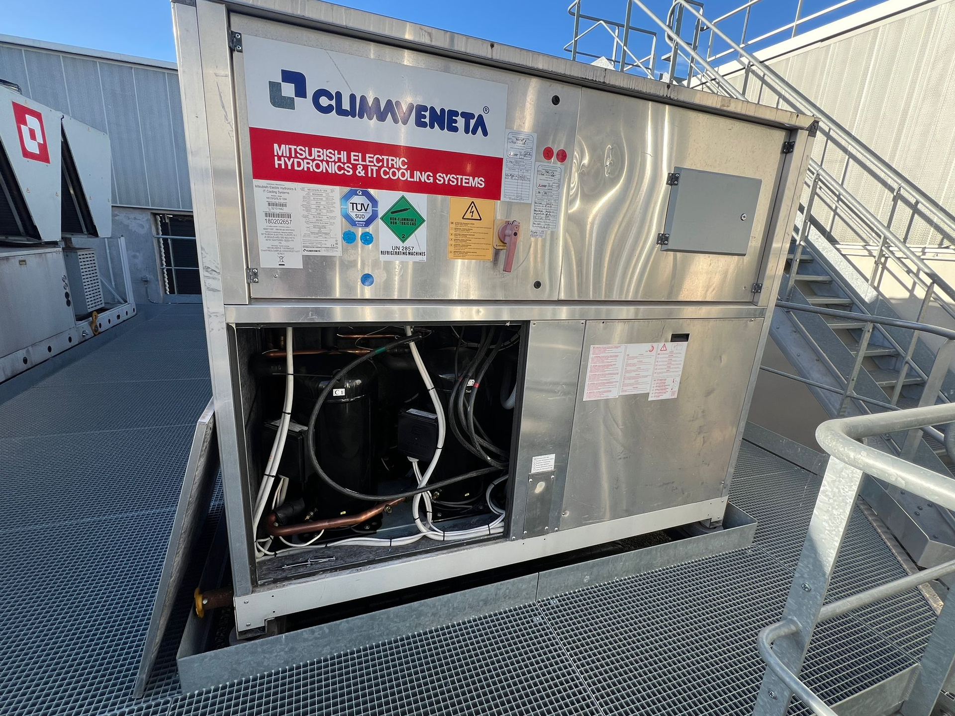 Unité de climatisation métallique sur un toit avec composants internes visibles, étiquette de marque 