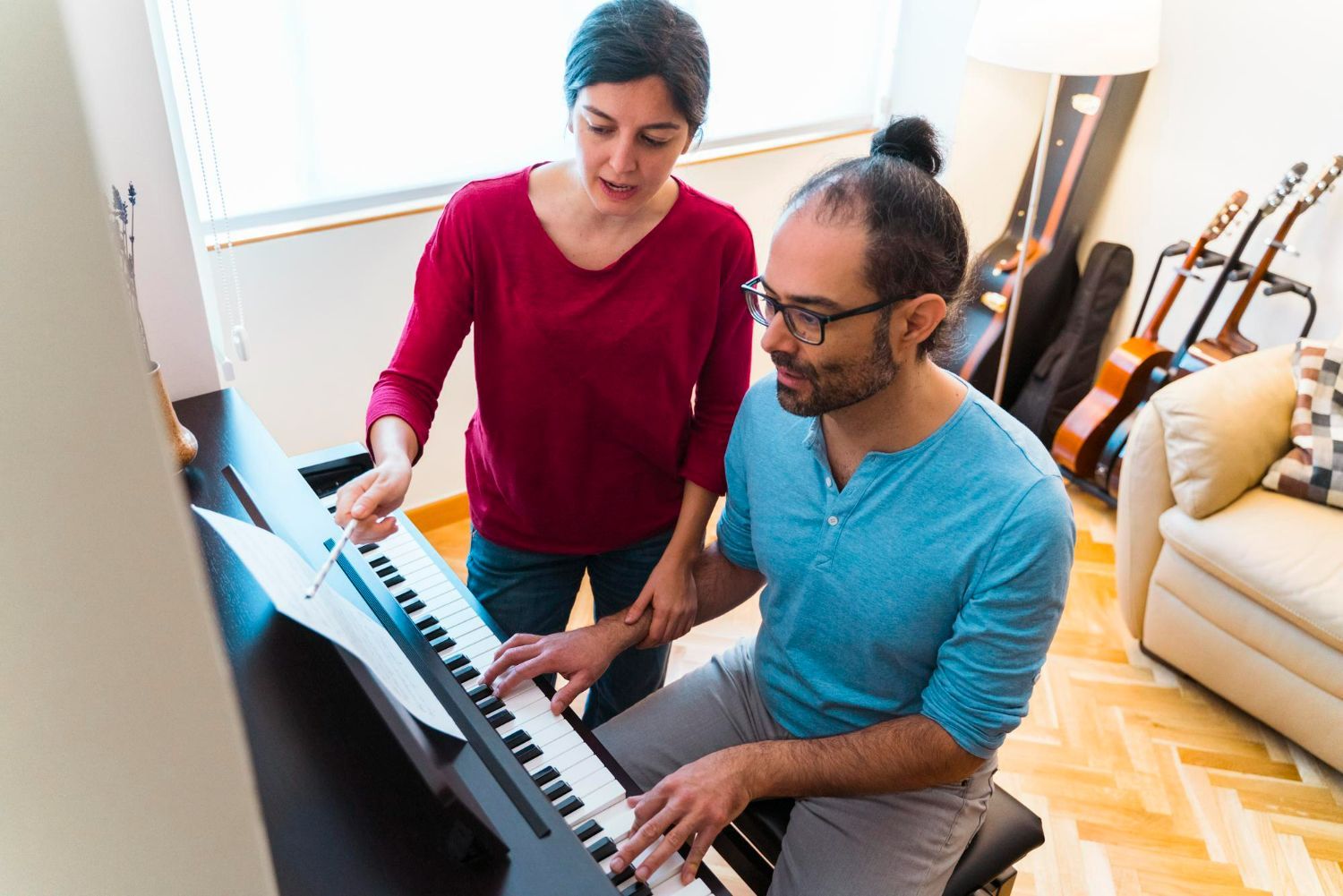 Woman teaching man to play piano; indoors.