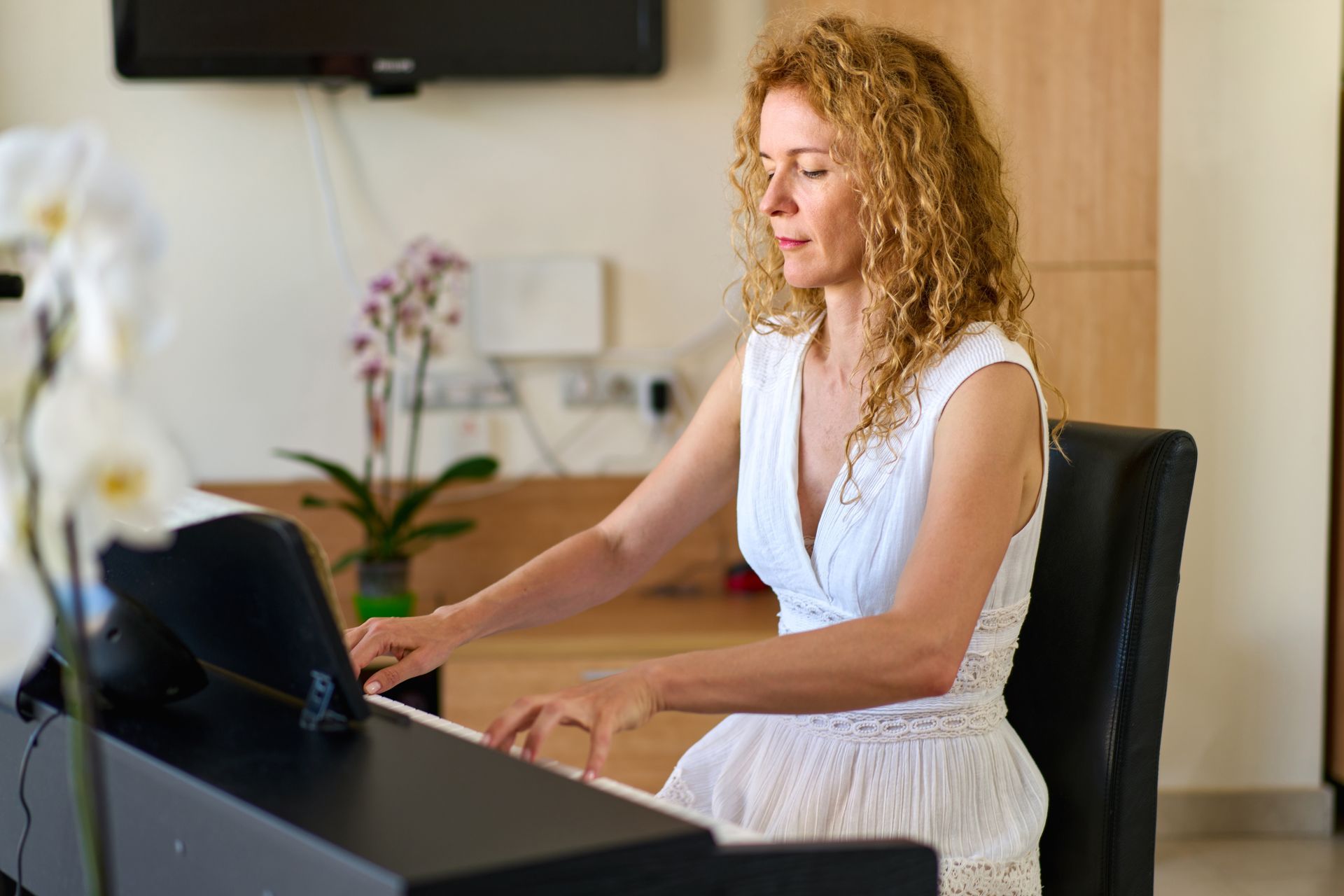 Woman in a white dress typing on a laptop at a desk in a modern office.