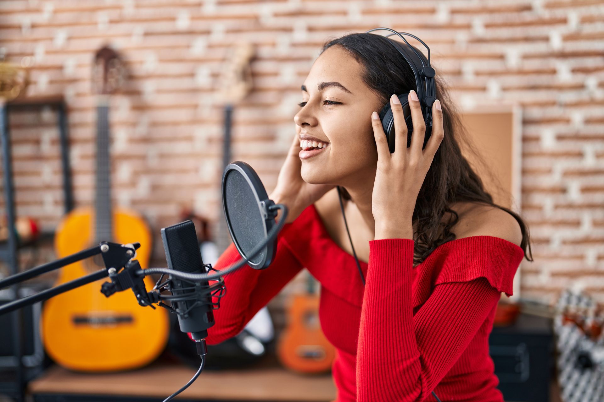 Singer in red sweater recording vocals in a studio with microphone and guitars in the background