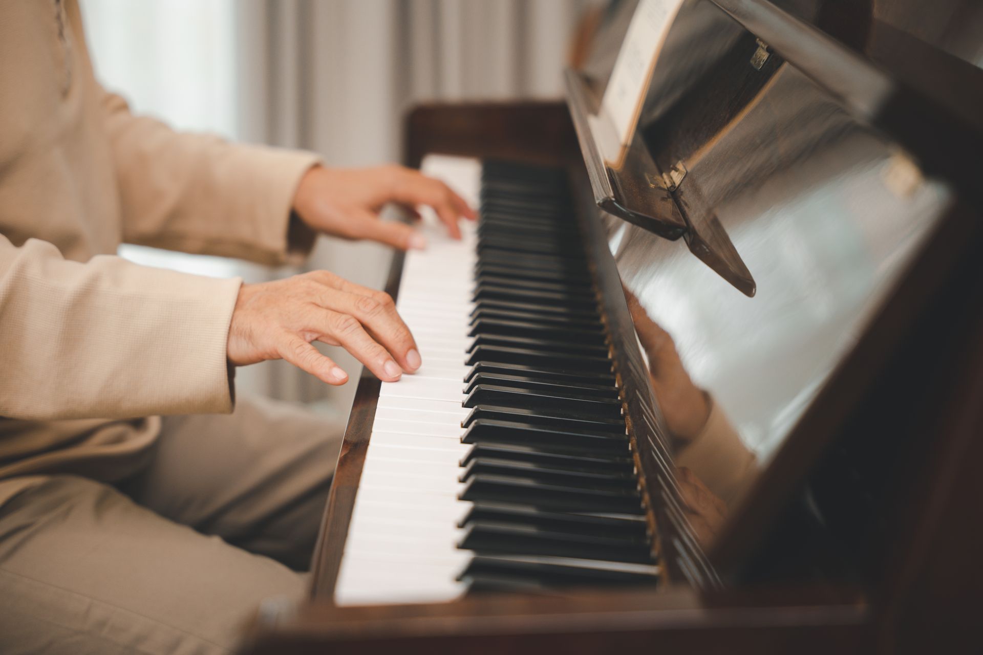 Person playing a piano, hands on the keys. Close-up view, warm lighting.