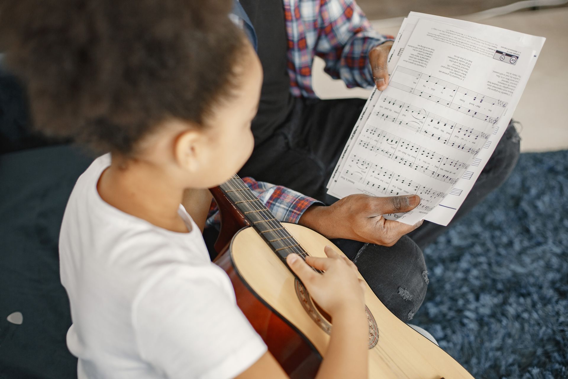 Adult and child reading sheet music together while the child holds a guitar.
