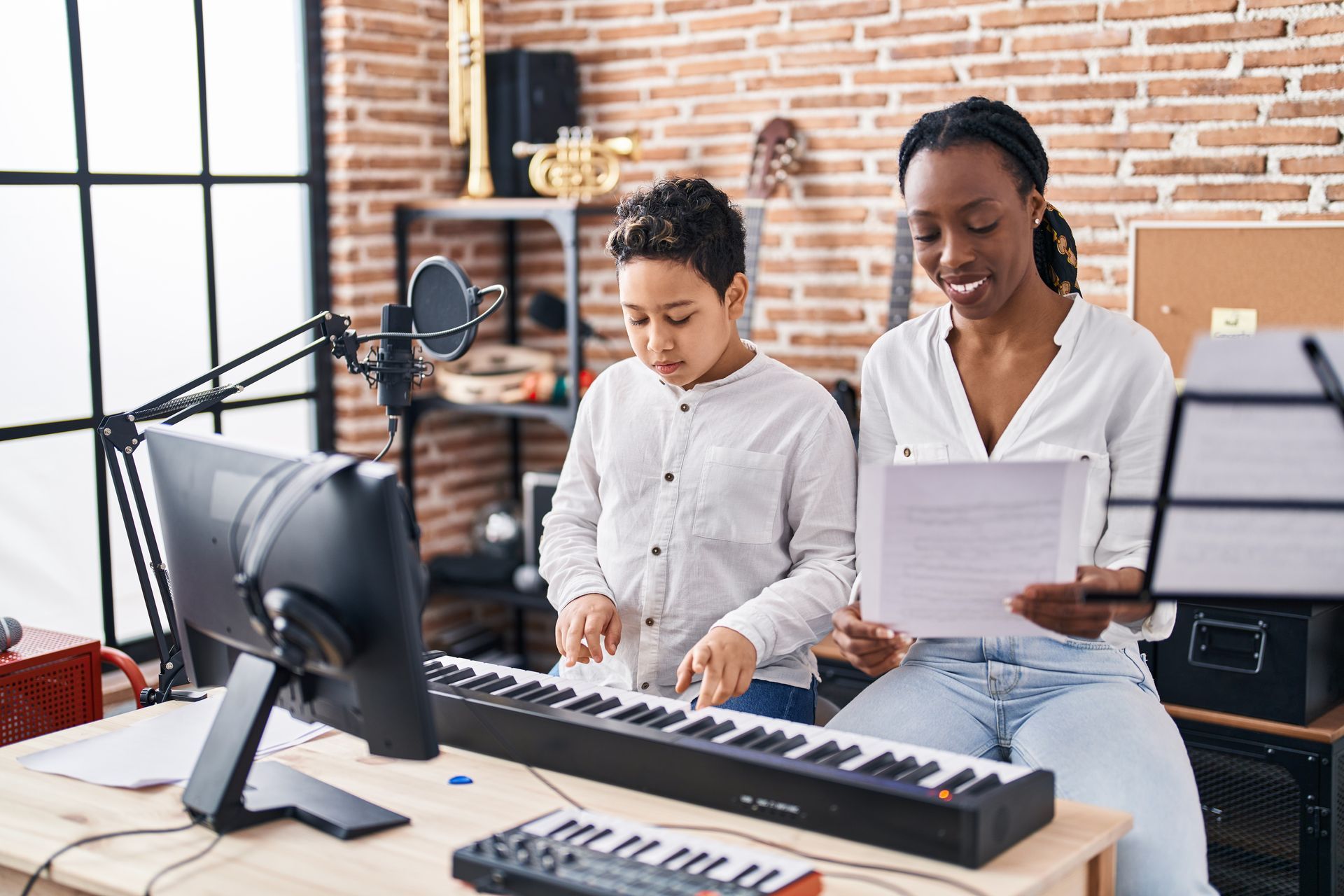 A woman and child playing a keyboard. Woman points at music sheets, looking at the child.