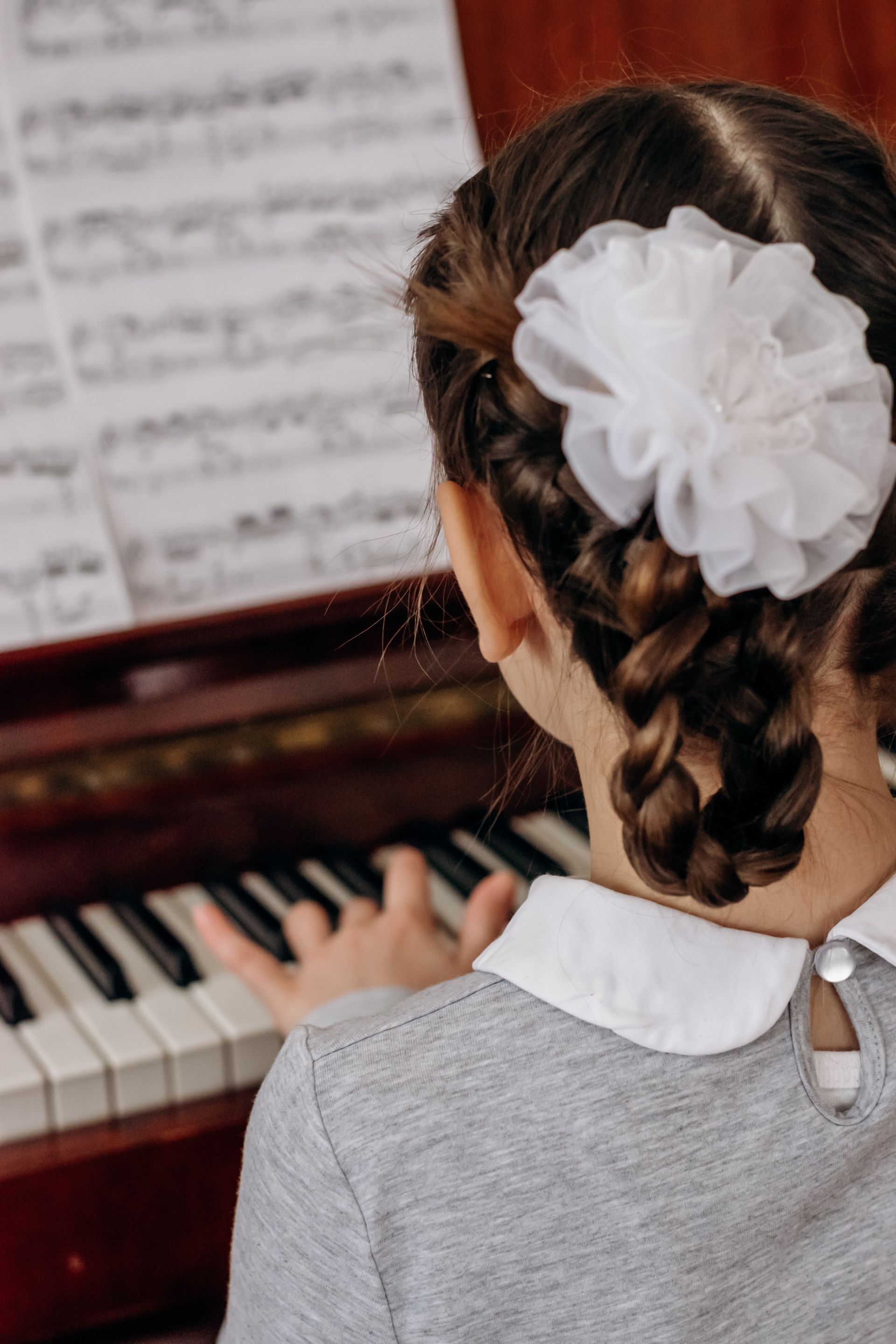 A little girl with a flower in her hair is playing a piano.