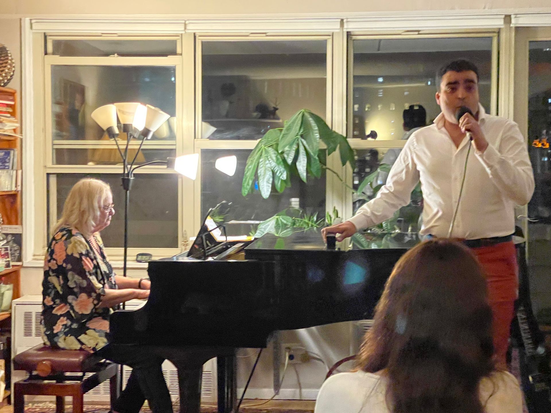 A man is singing into a microphone while a woman plays a piano