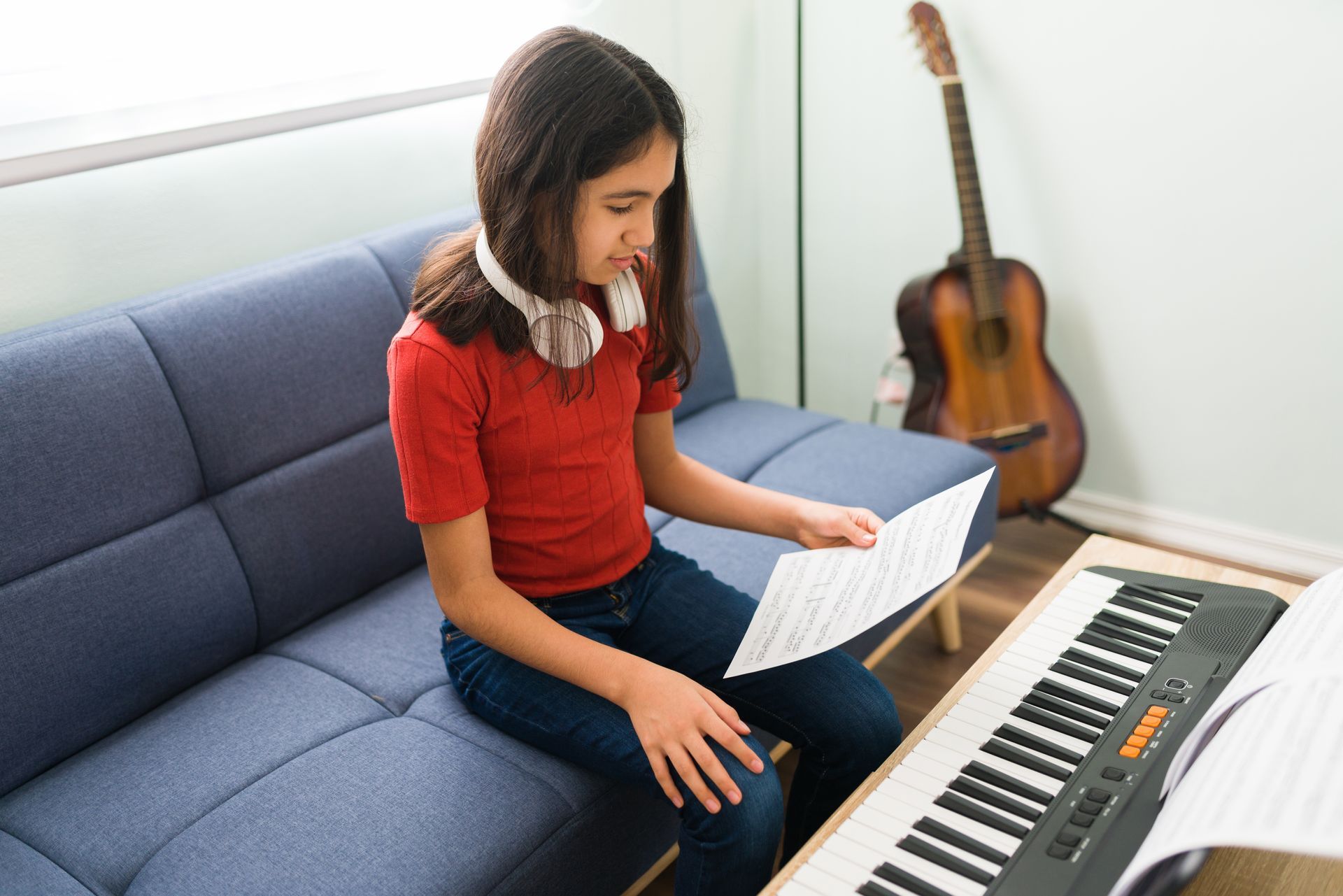 A young girl is sitting on a couch playing a keyboard.