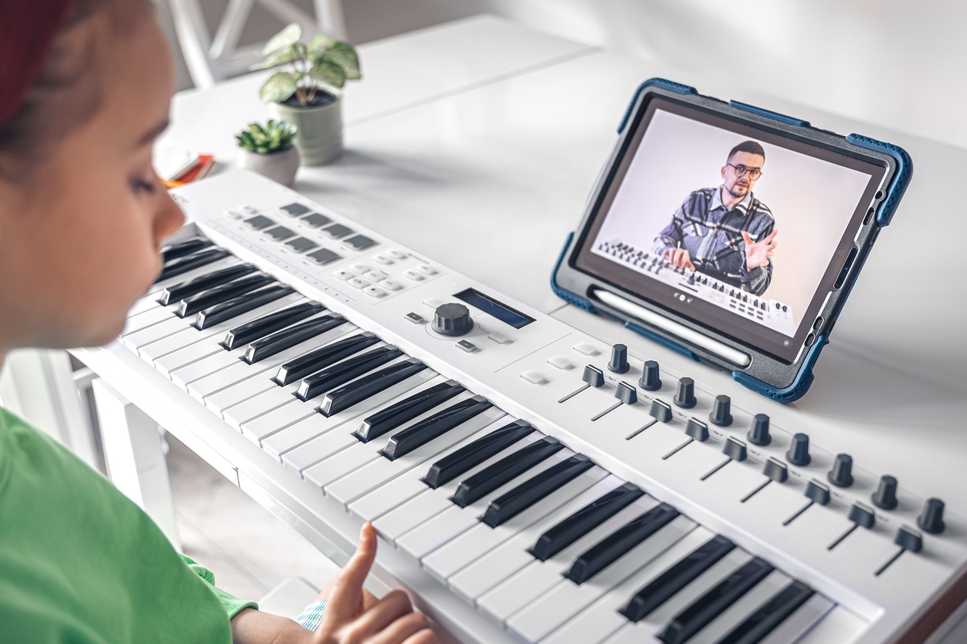 A young girl is playing a piano while watching a video on a tablet.
