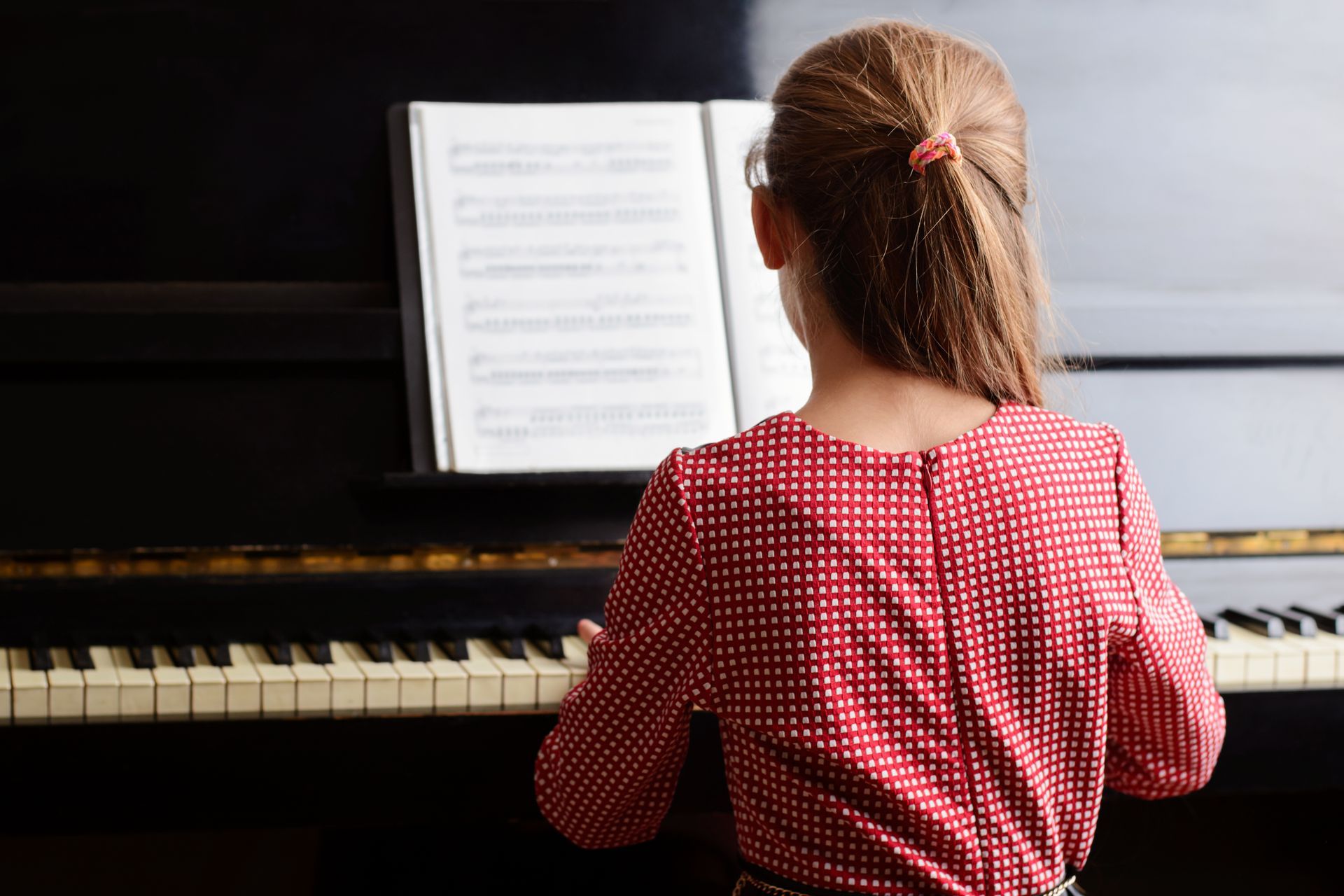 A young girl is sitting at a piano with an open book.