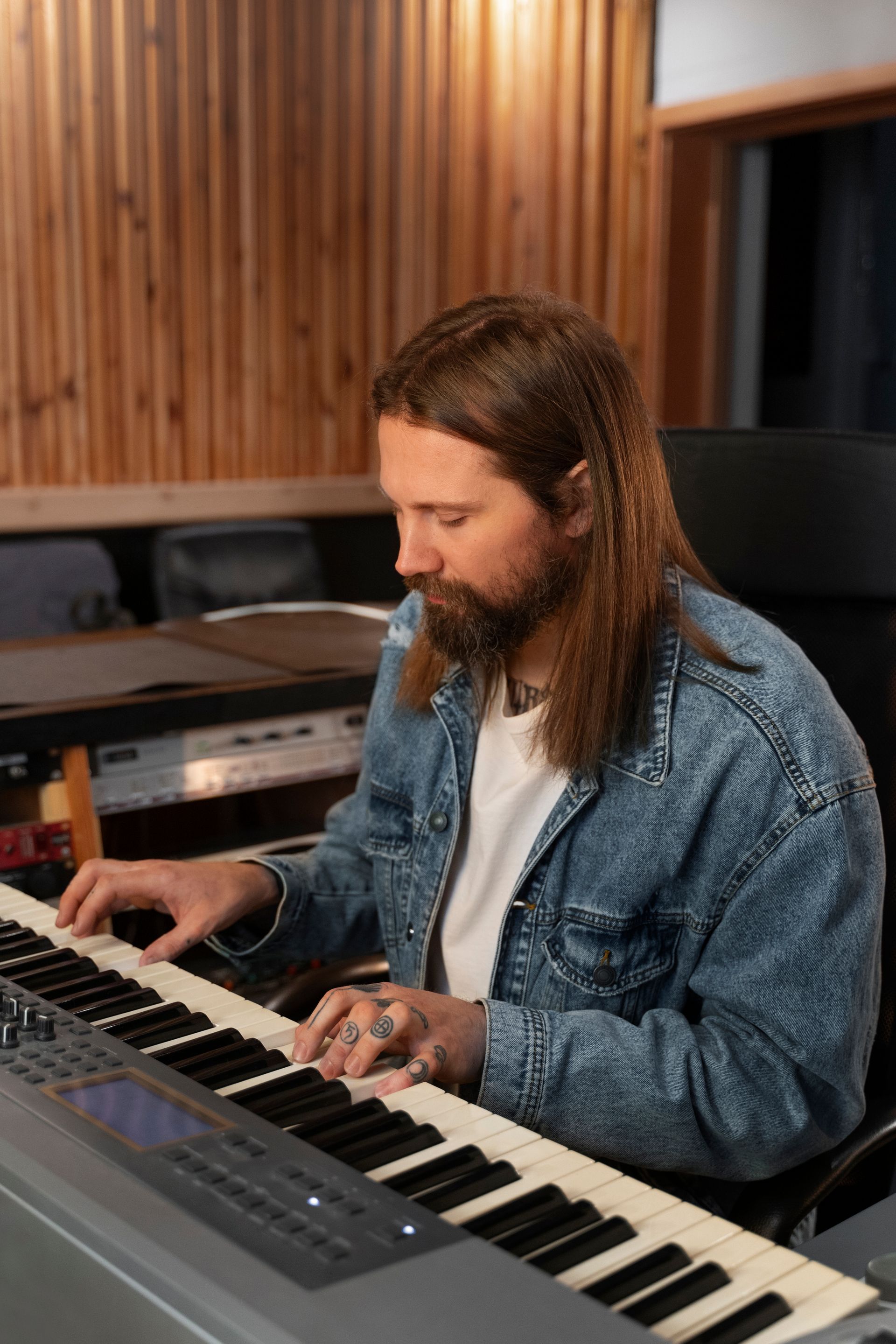 A man with long hair and a beard is playing a piano in a recording studio.