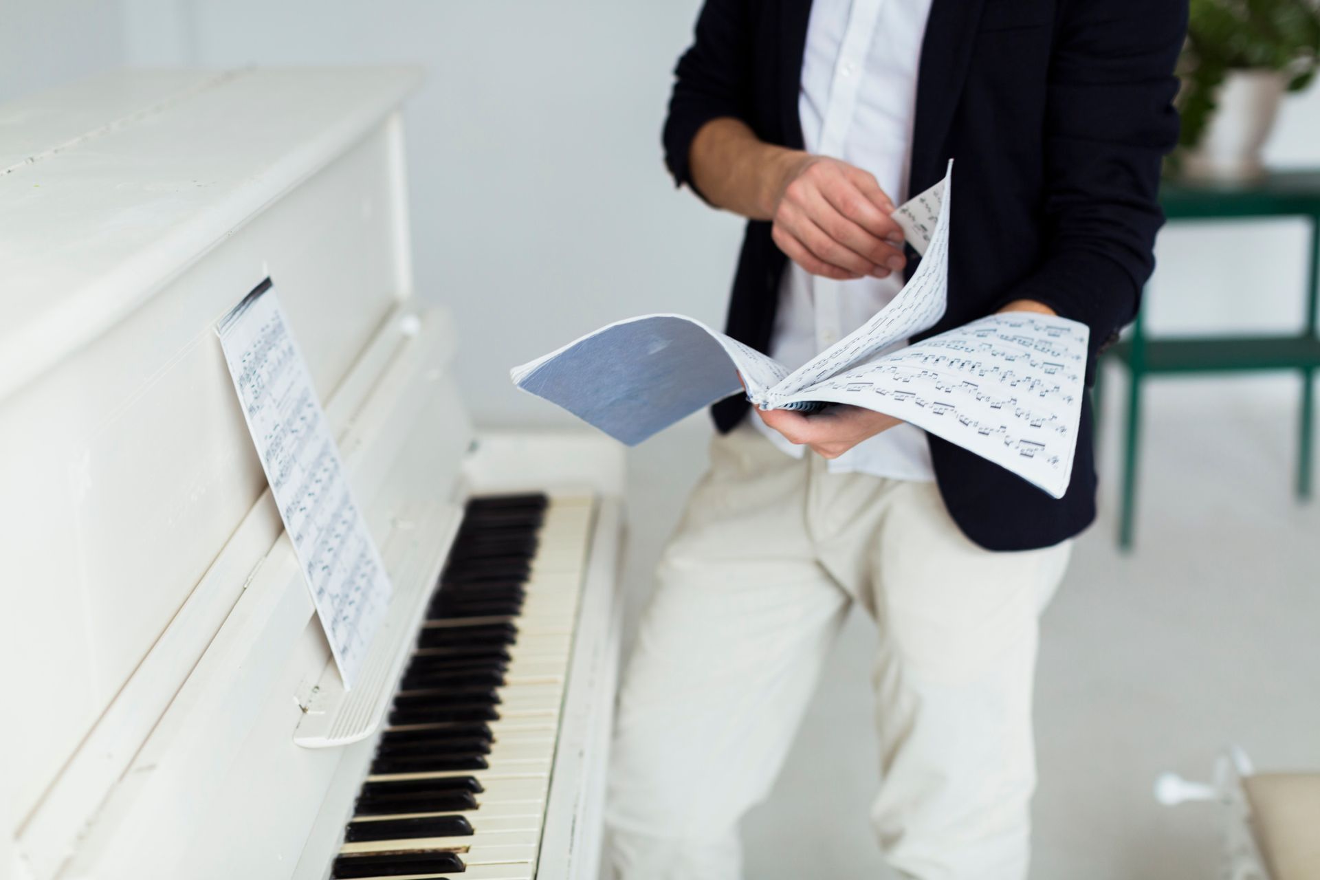 A man is sitting at a white piano looking at sheet music.