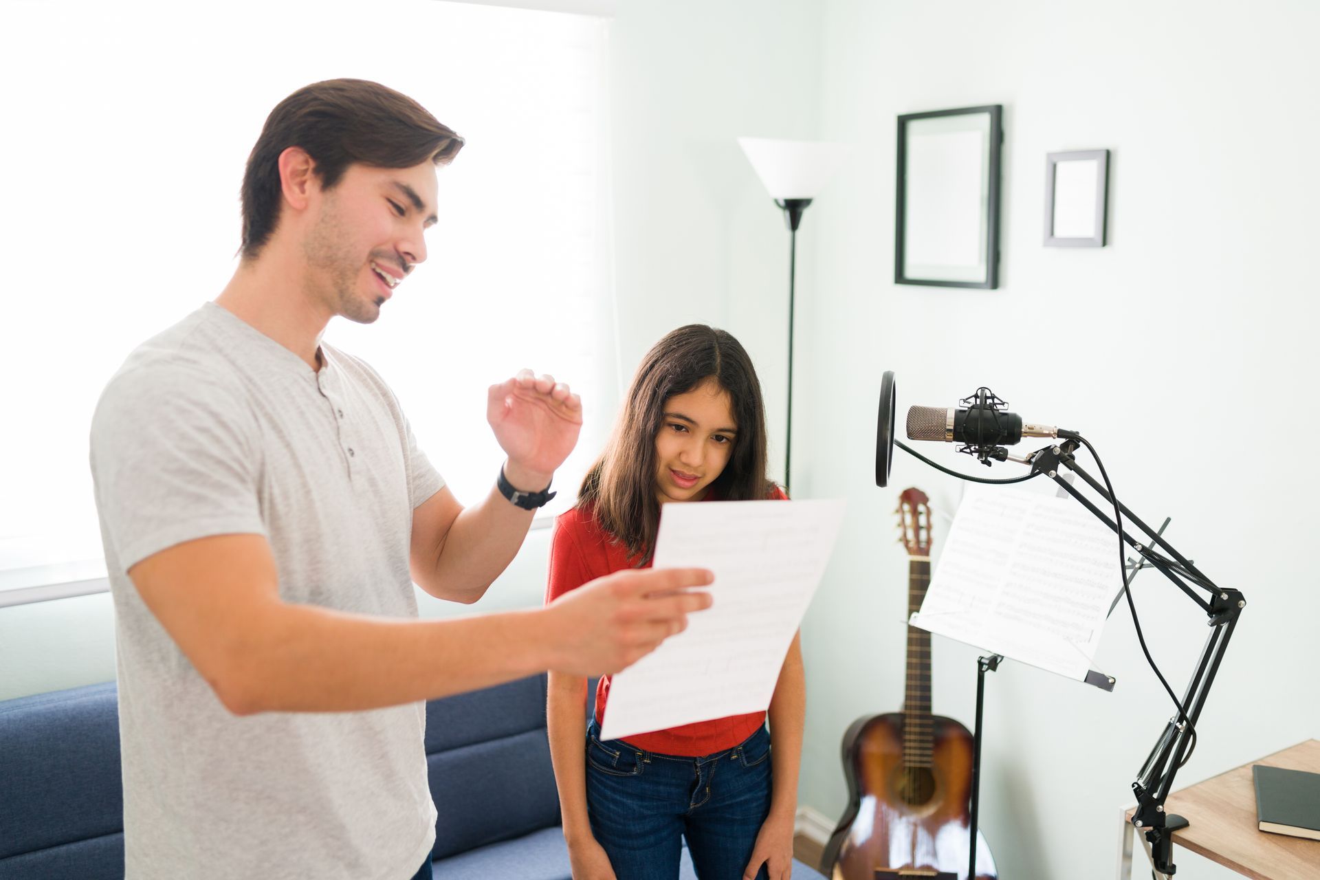 A man is teaching a girl how to sing in front of a microphone.