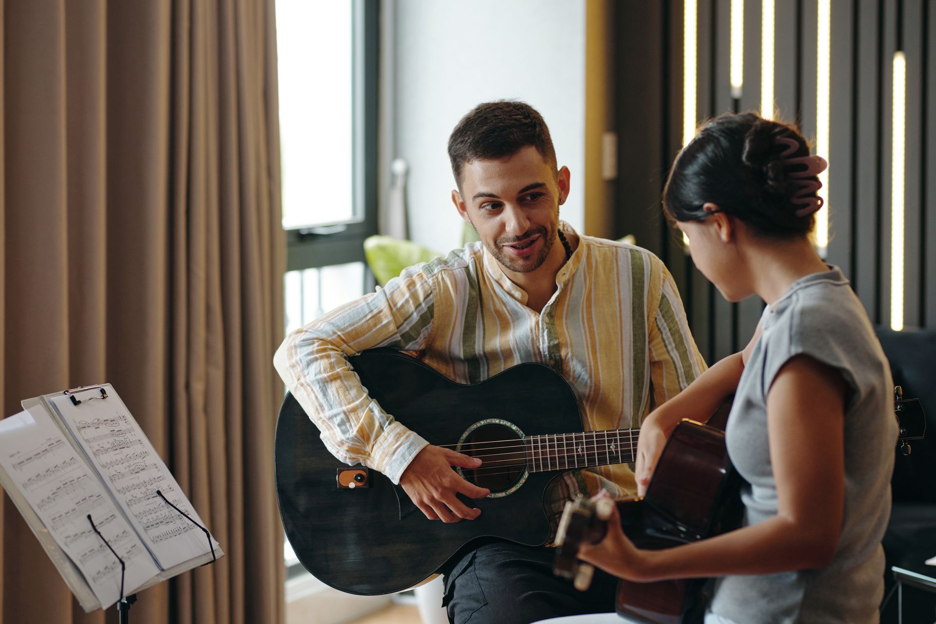 A man is teaching a woman how to play an acoustic guitar.