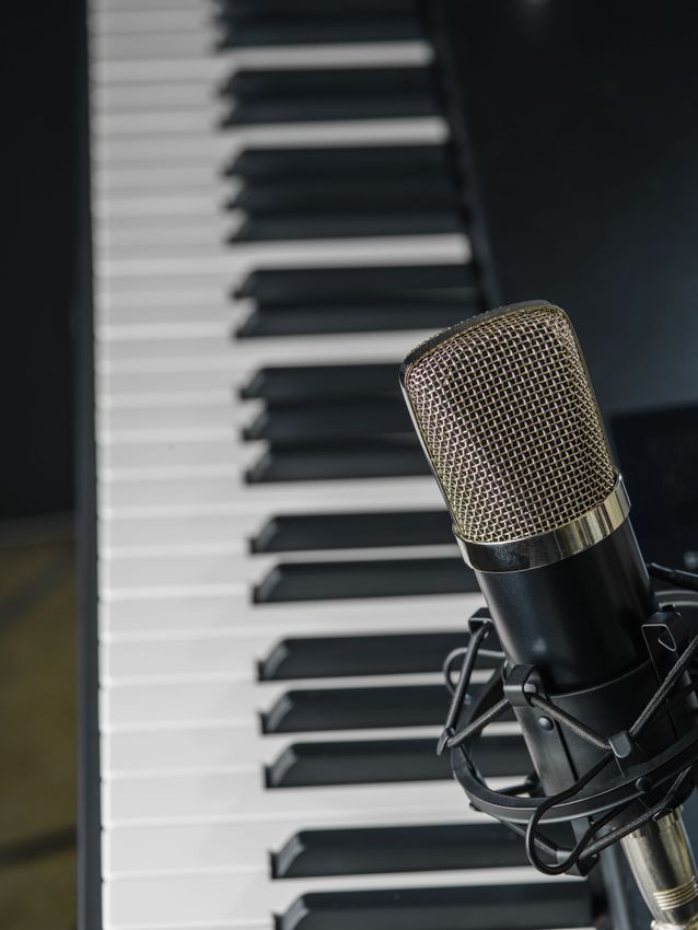 Microphone on a stand beside piano keys in a dark studio setting