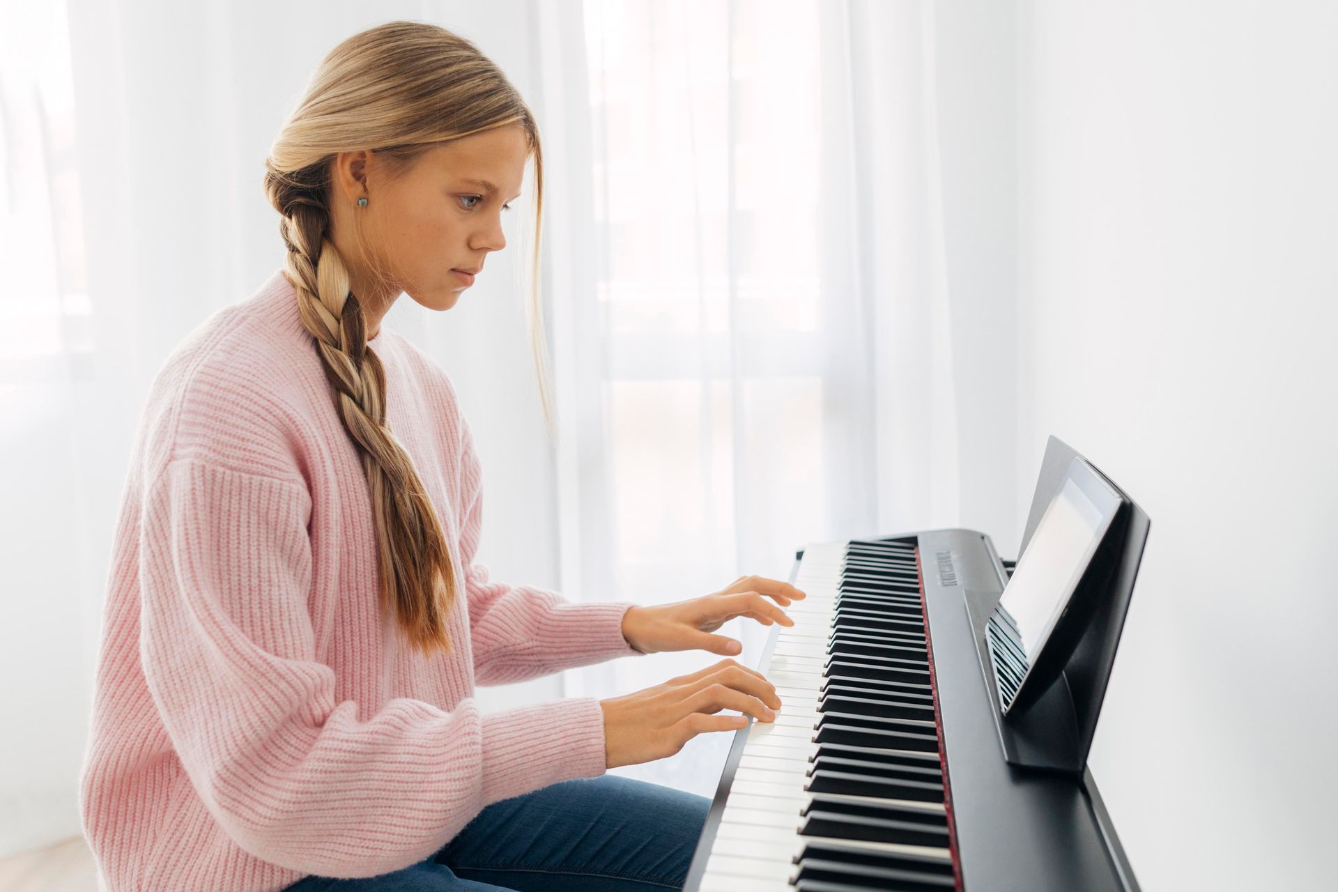 A young girl in a pink sweater is playing a piano.