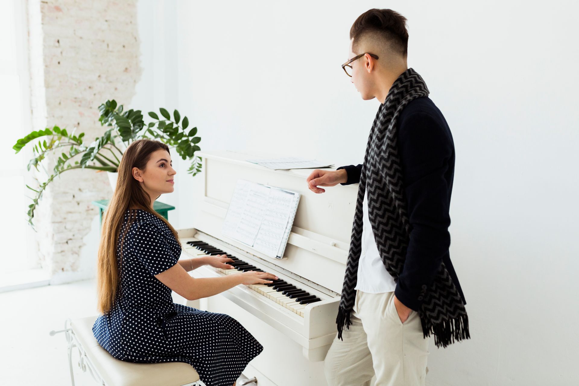 A man is standing next to a woman playing a piano.