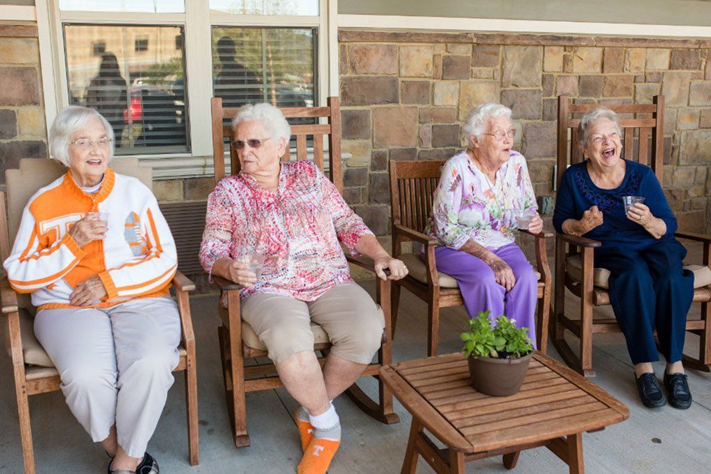 A group of elderly women are sitting in rocking chairs on a porch.