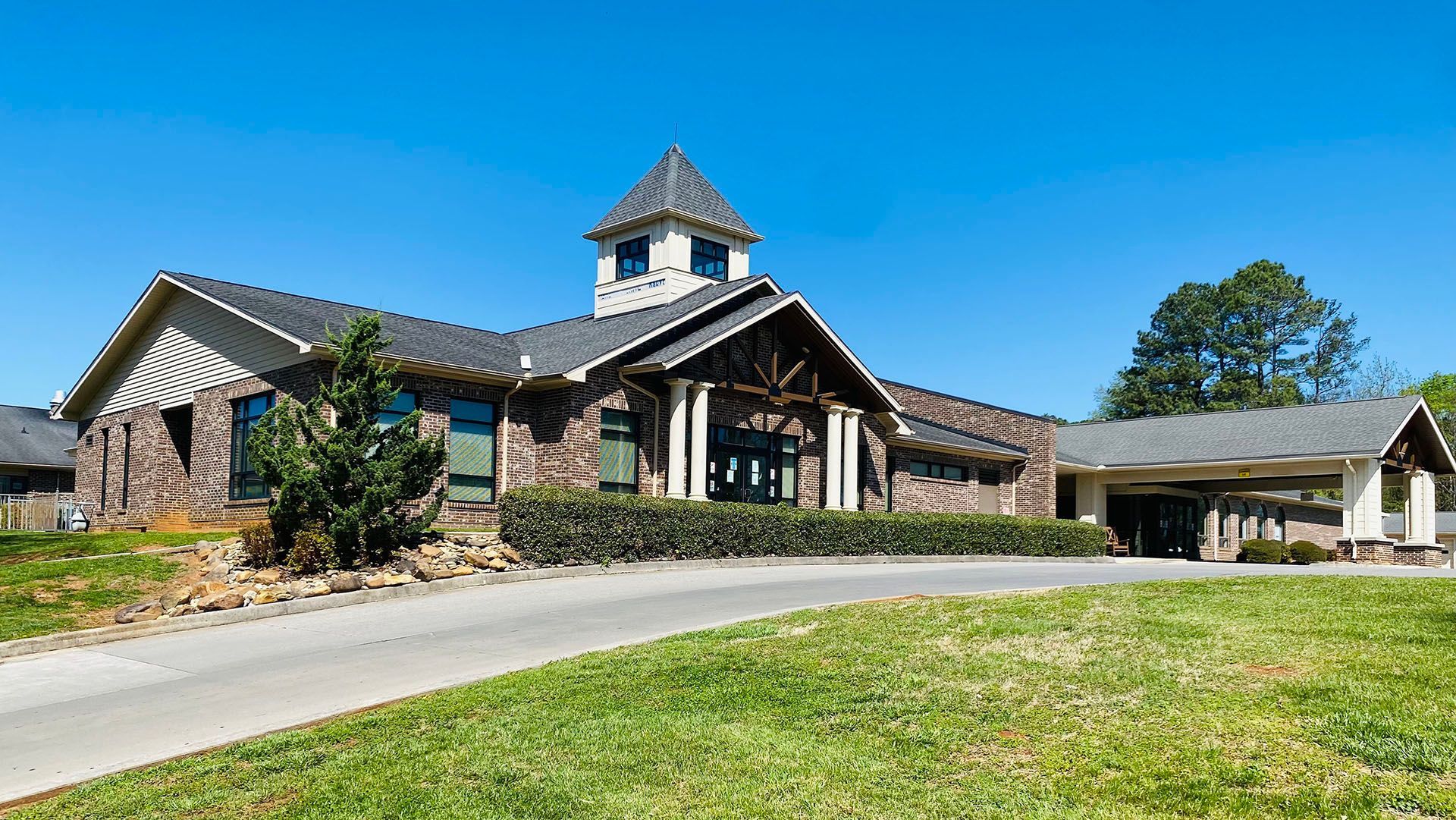 A large house with a clock tower on top of it is sitting on top of a lush green hill.