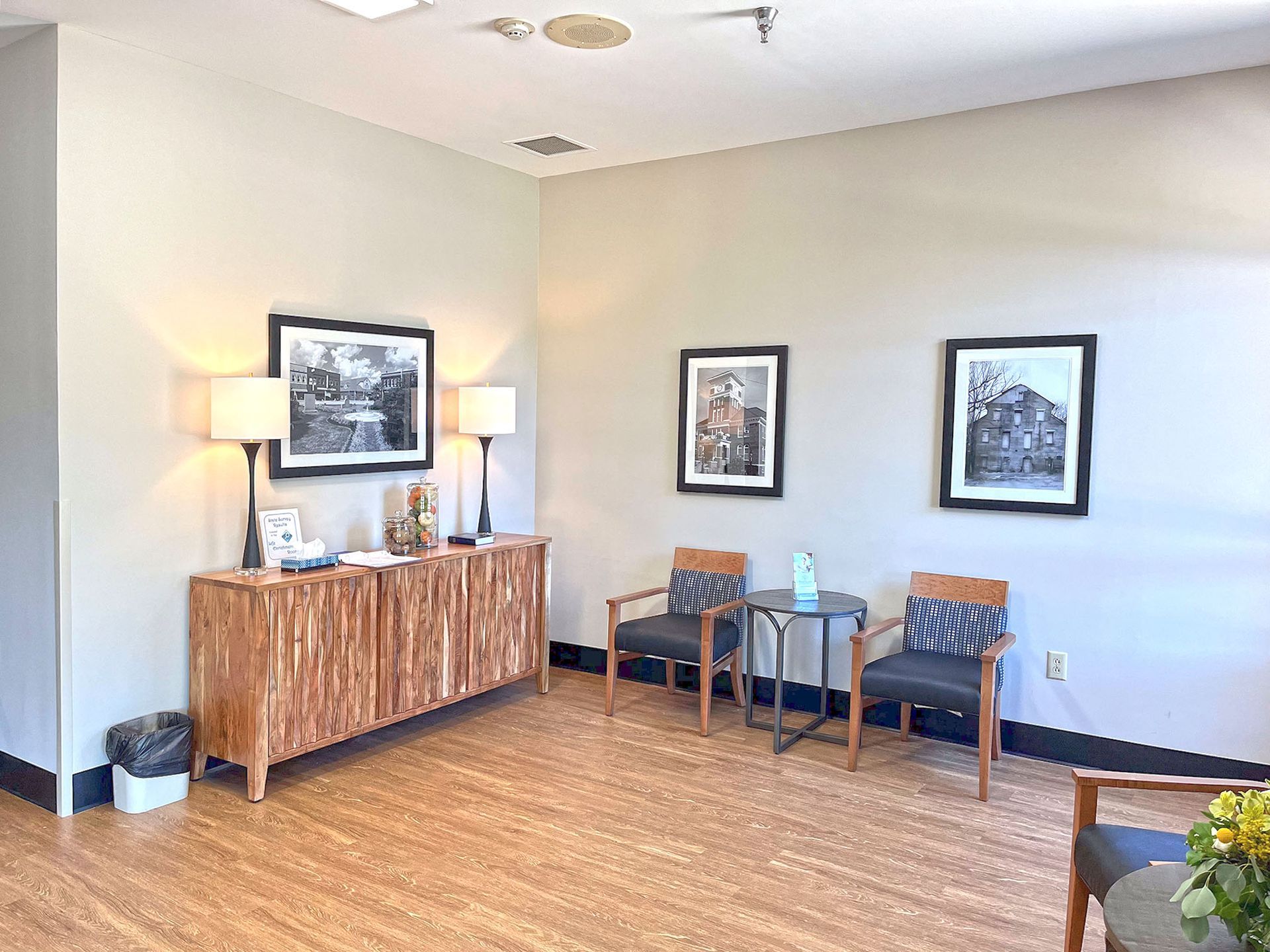 A waiting room with a wooden cabinet , chairs , tables and pictures on the wall.