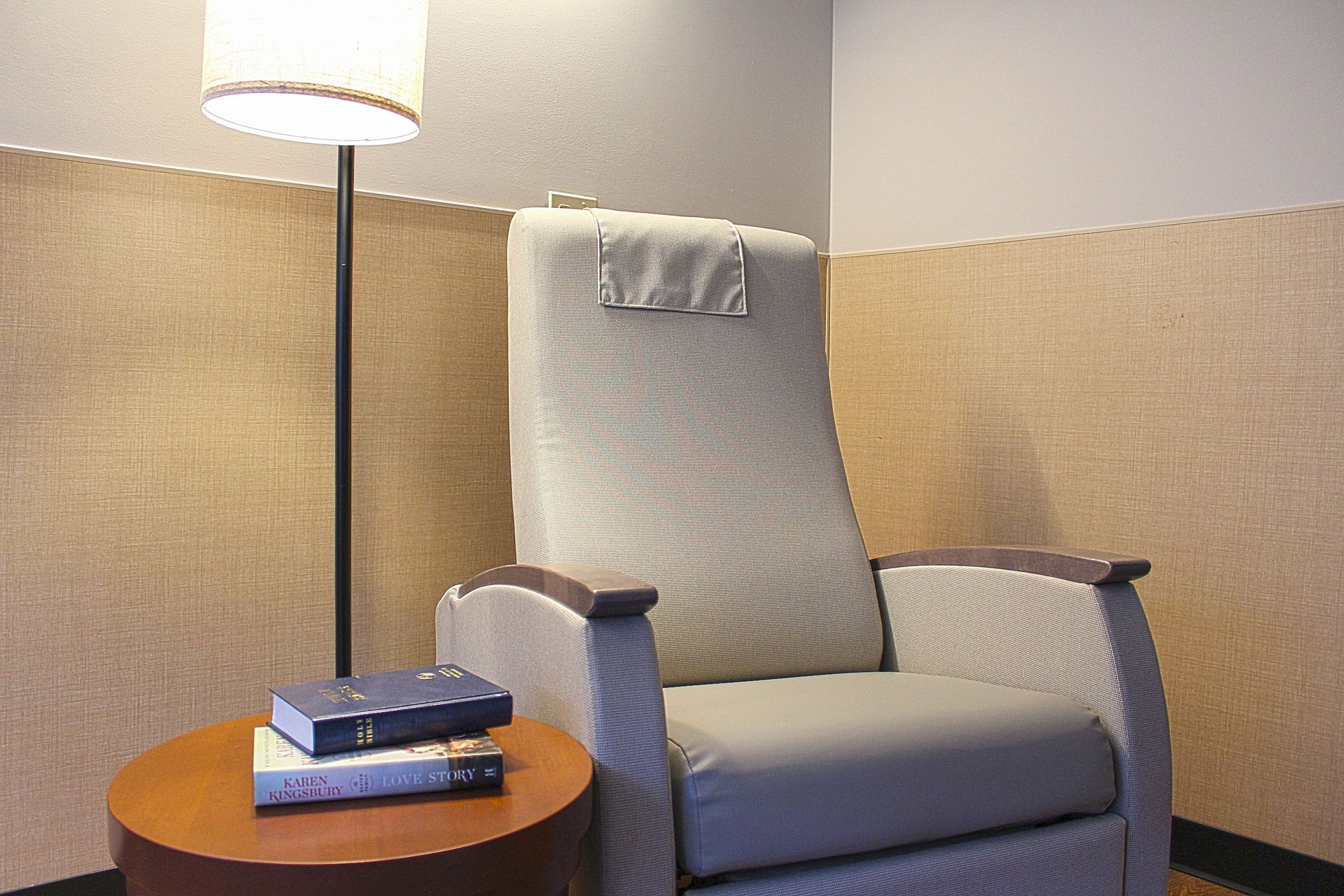 A chair is sitting next to a lamp and a table with books on it.