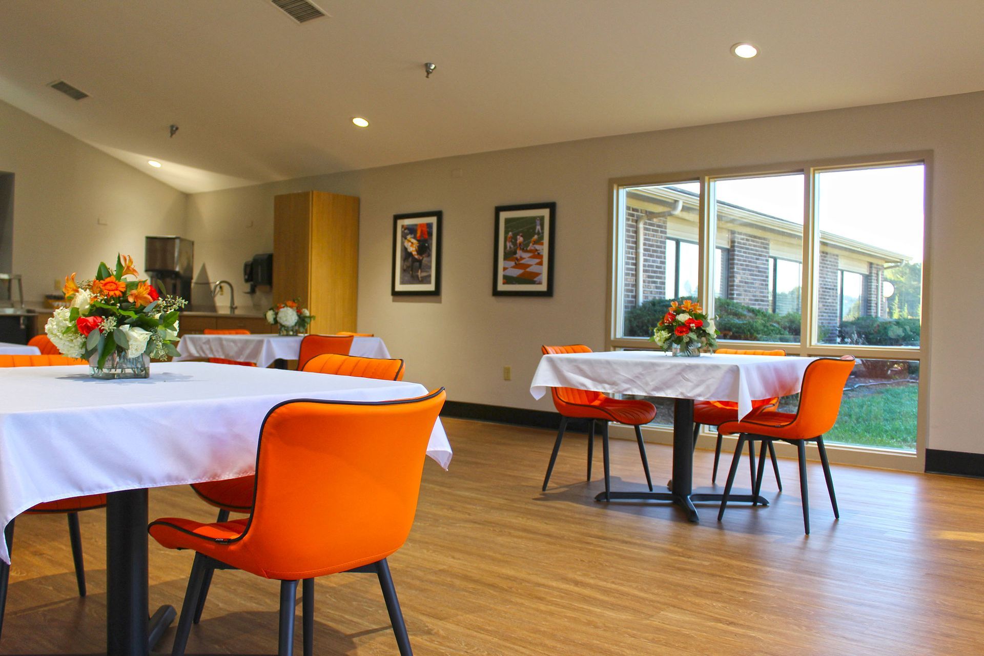 A dining room with tables and chairs and a vase of flowers on the table.
