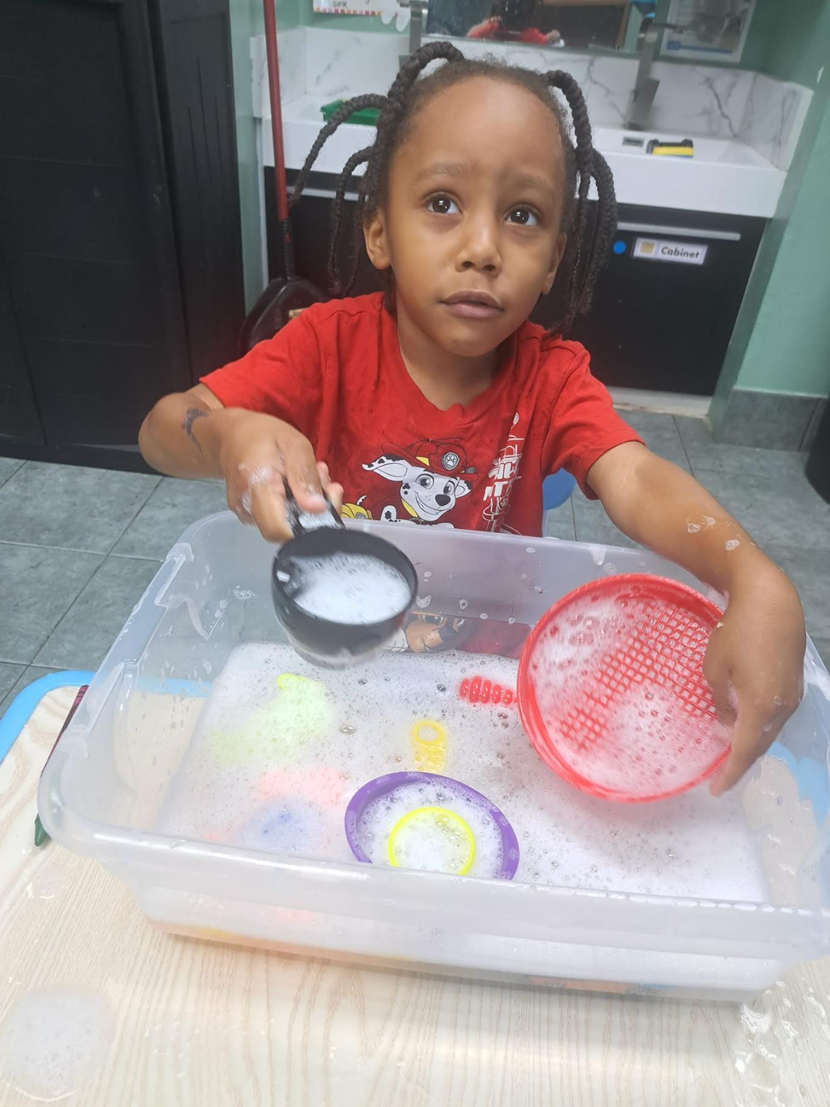 A young boy is pouring soap into a plastic container.