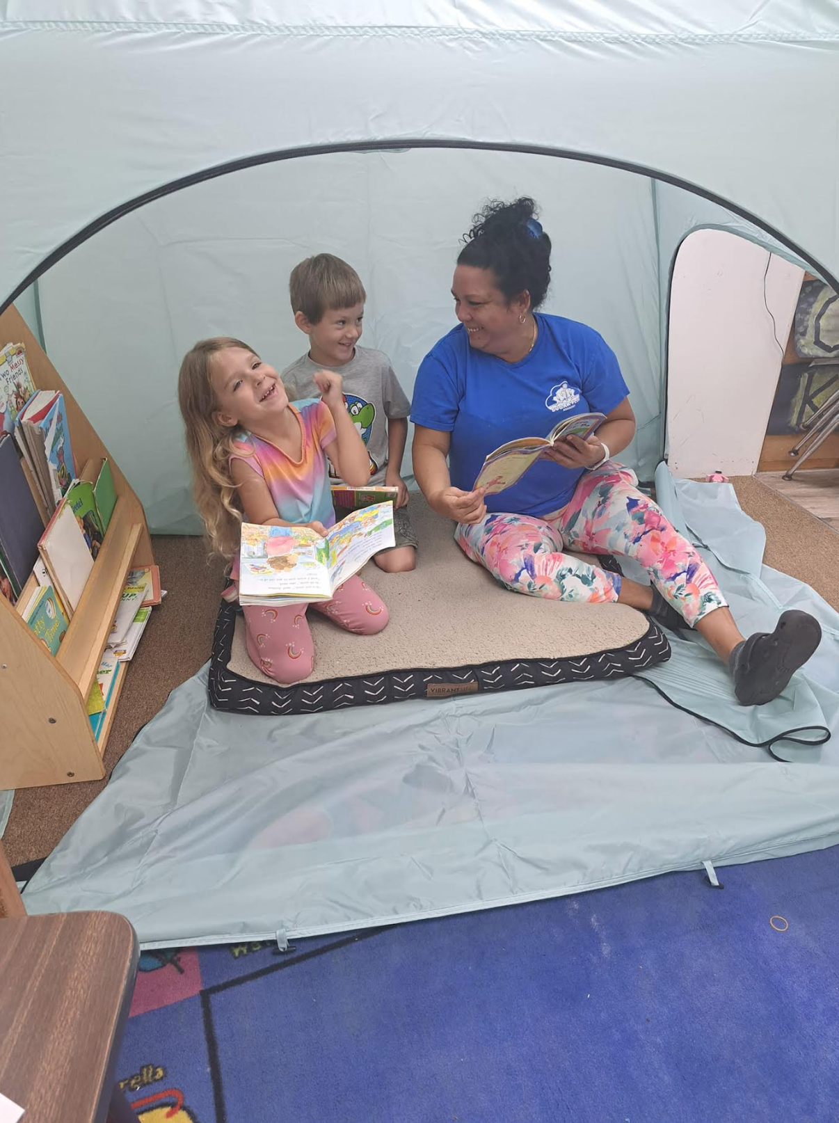 A woman is reading a book to two children in a tent.