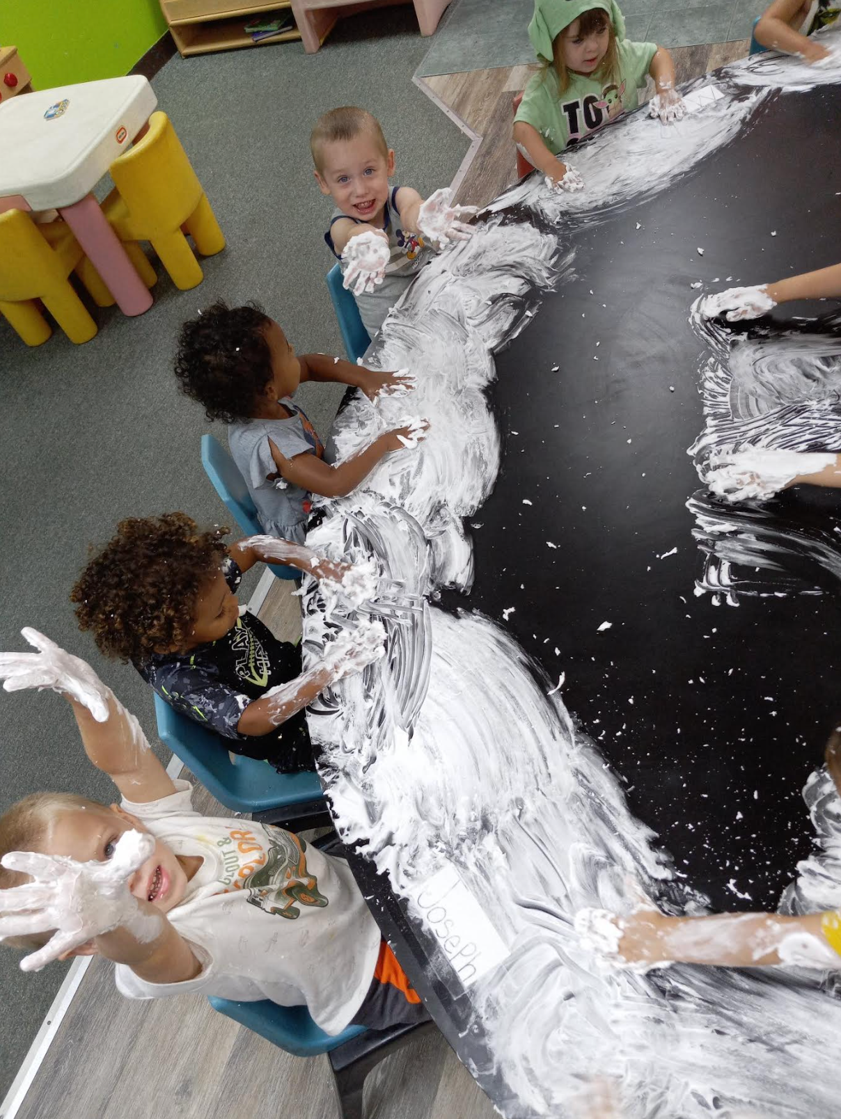 A group of children are playing with shaving cream on a table