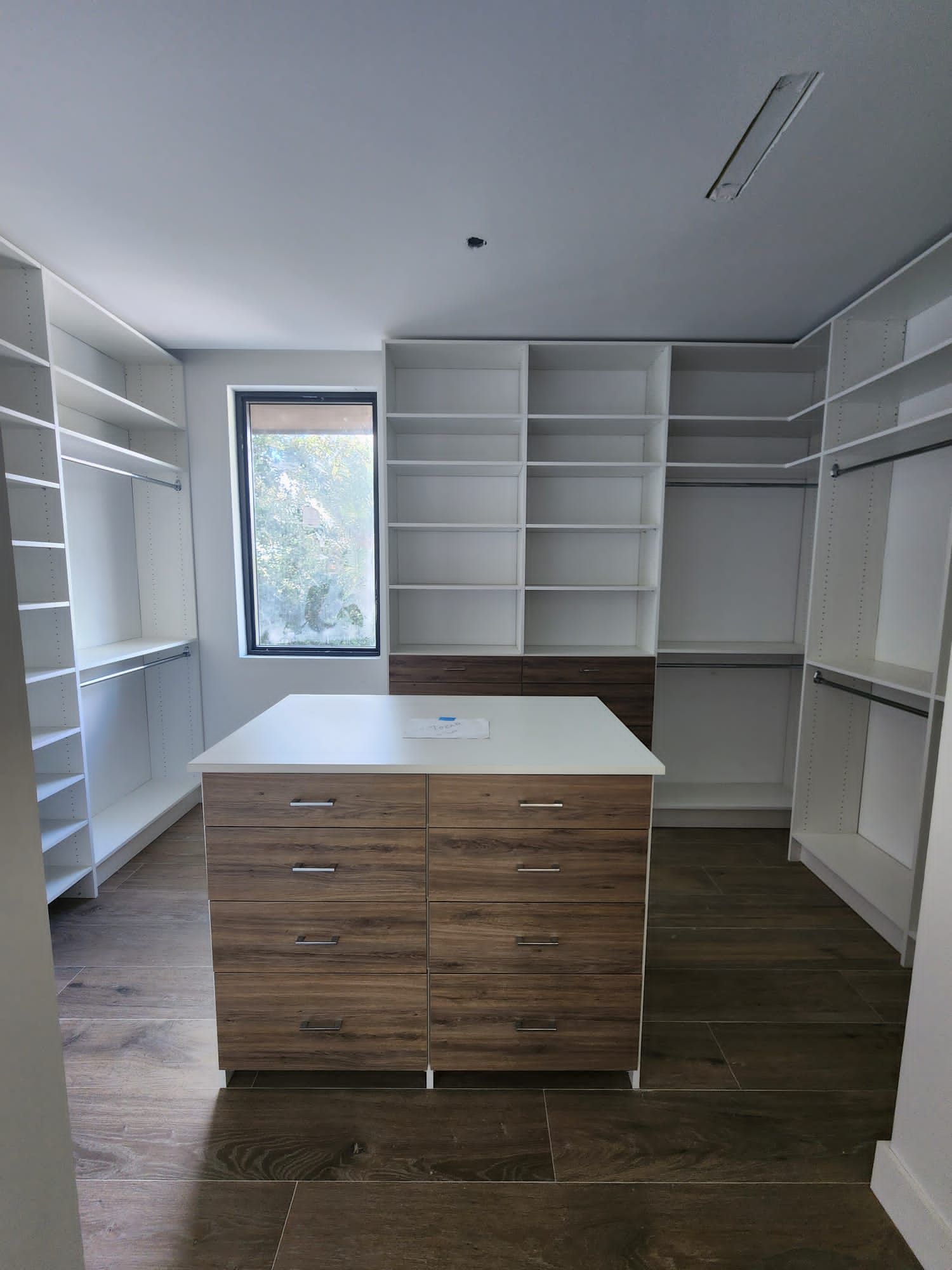 A walk in closet with lots of shelves and drawers and a large island in the middle.