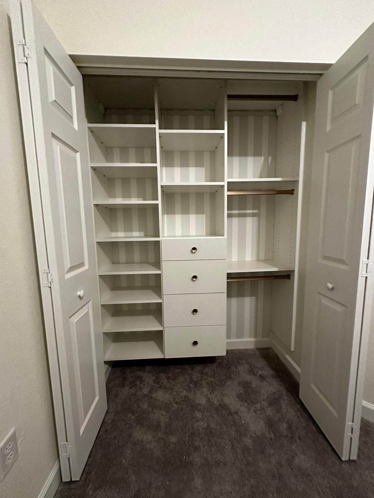A kids closet with shelves , drawers , and a striped wall.